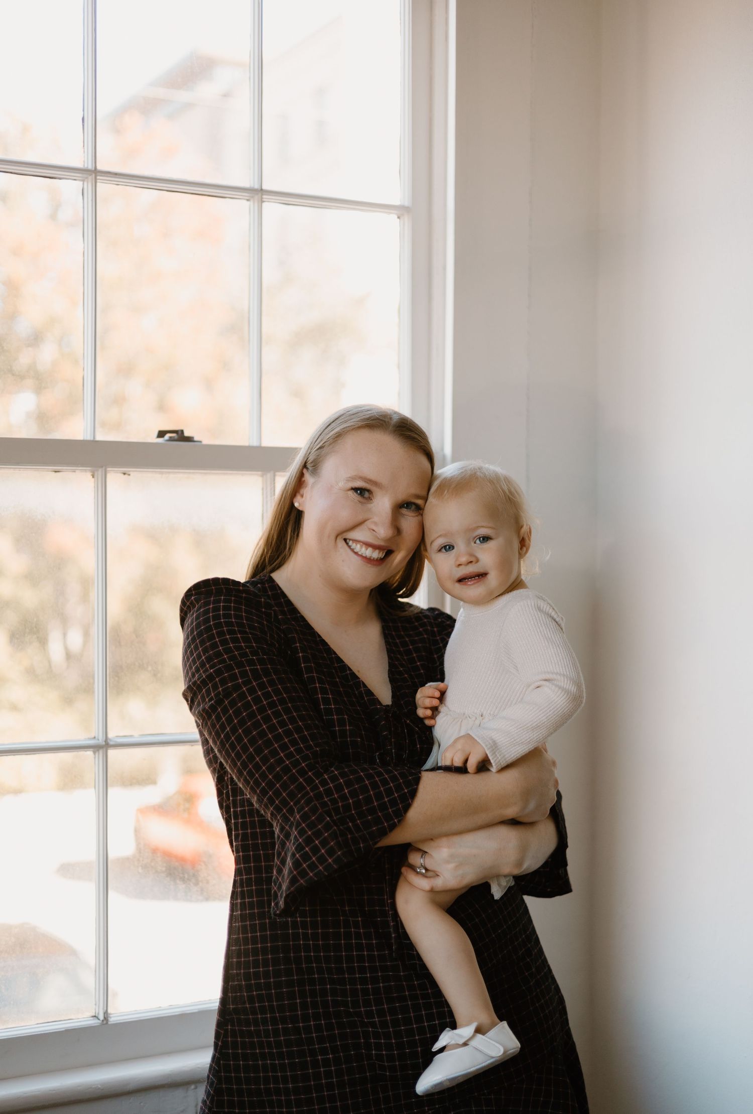 A parent and baby share joyful moments by a bright window.
