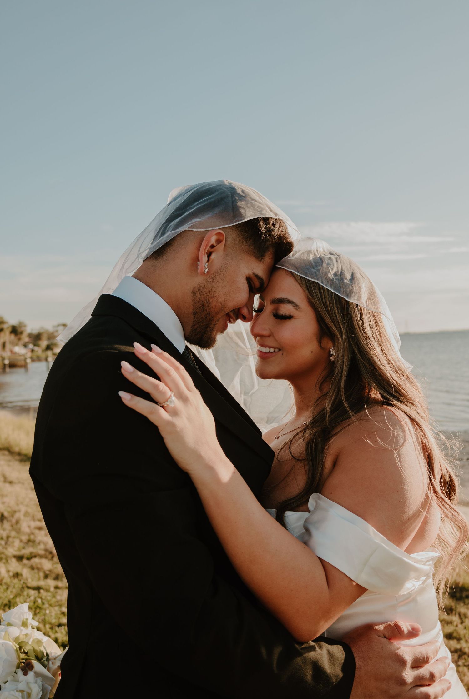 Couple in wedding attire embracing on beach during sunset photoshoot.