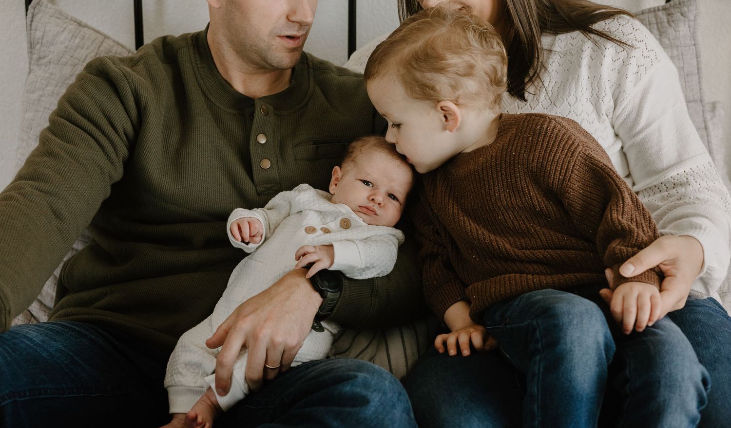 Parents in casual wear holding newborn baby during indoor lifestyle session.