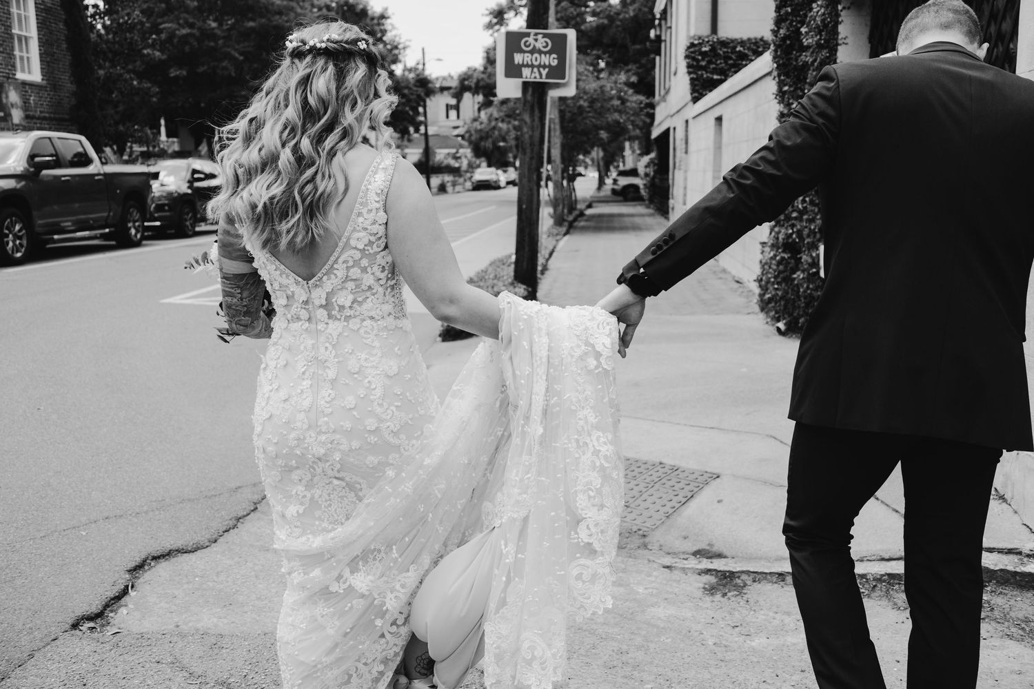 A couple in wedding attire walks together on a city street in black and white.