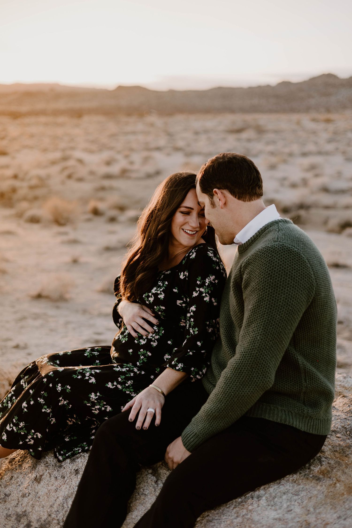 Desert maternity session at sunset with couple in black dress and green sweater.