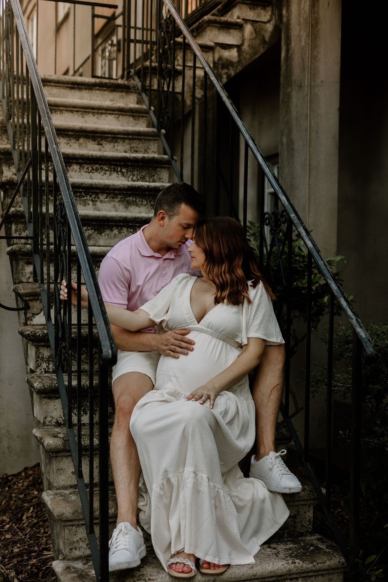 A couple sits on stone steps sharing an intimate moment in casual white attire.