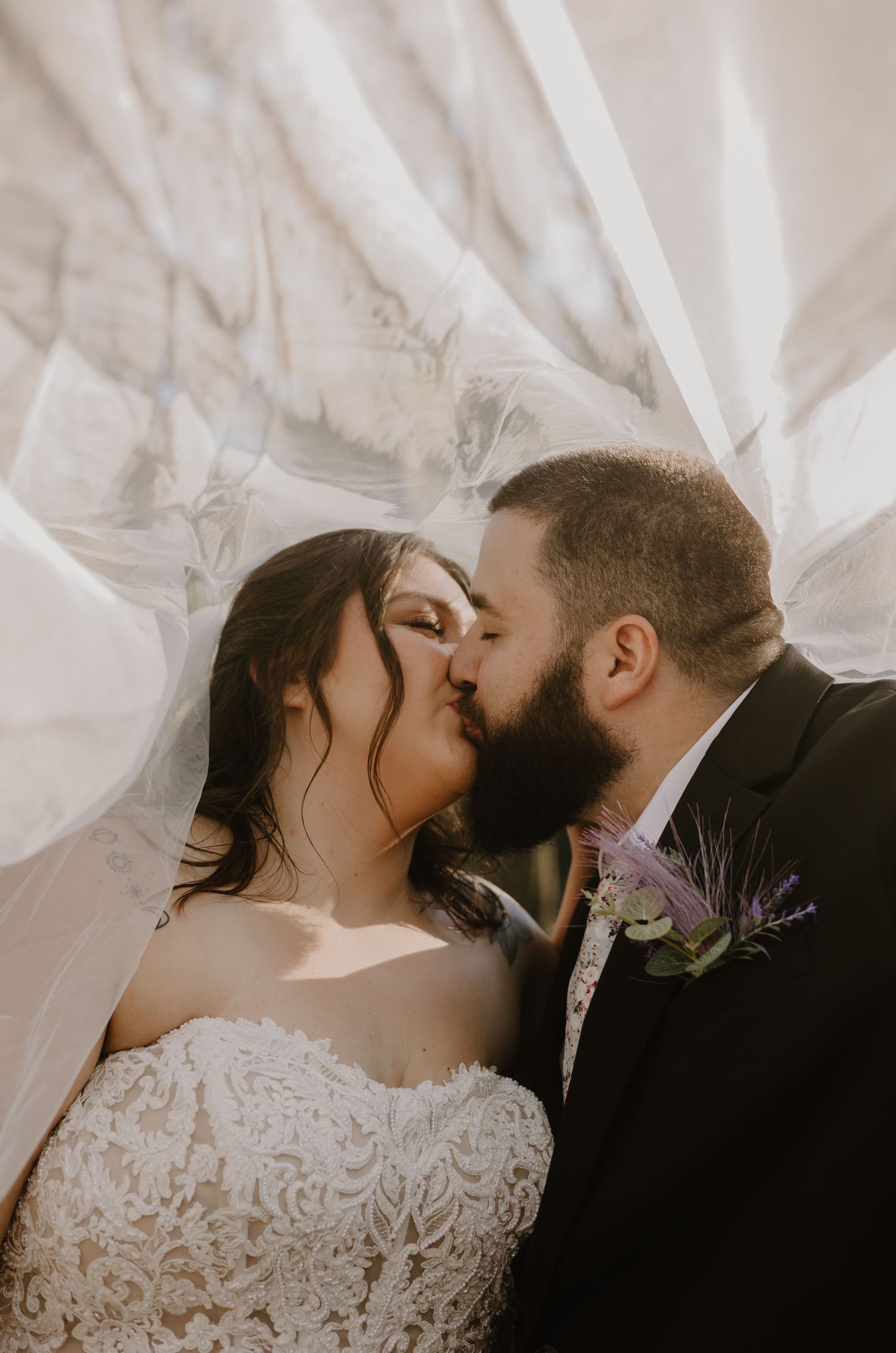 Romantic wedding portrait with flowing veil and intimate kiss.