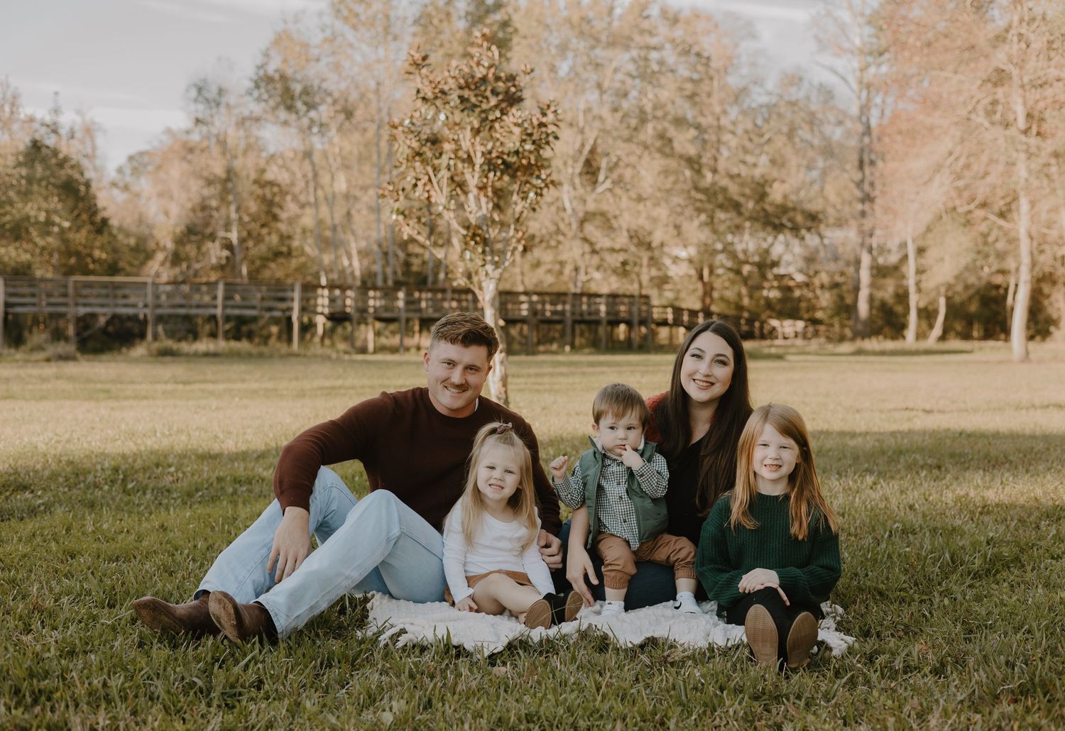 Family lying together on grass during outdoor portrait session at sunset.
