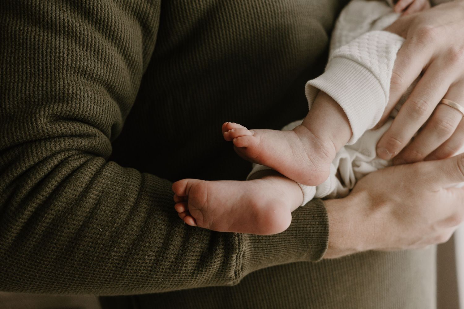 Intimate close-up of hands holding newborn baby in dark and light tones.