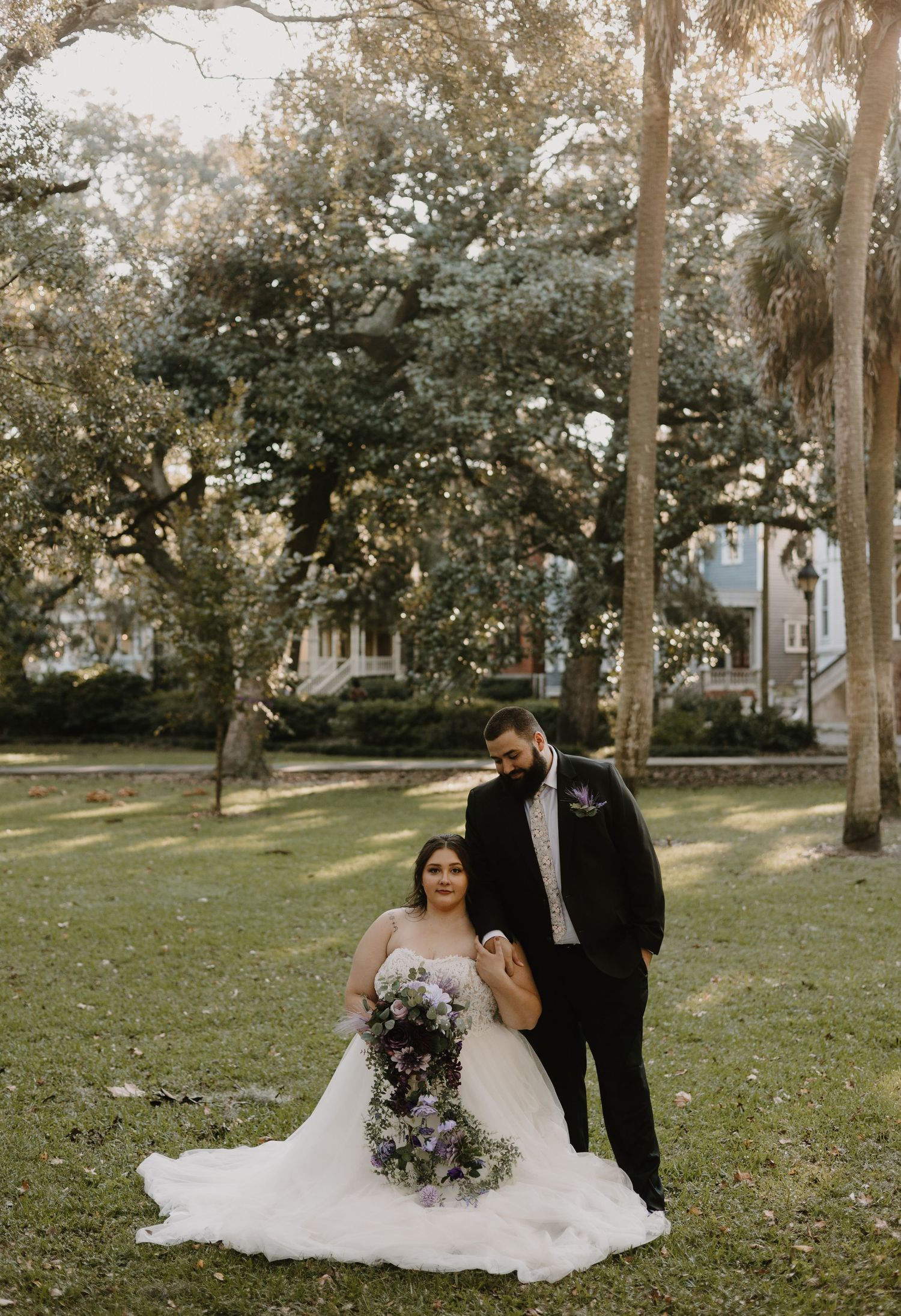 Elegant wedding couple poses in park with flowing white dress and autumn scenery.