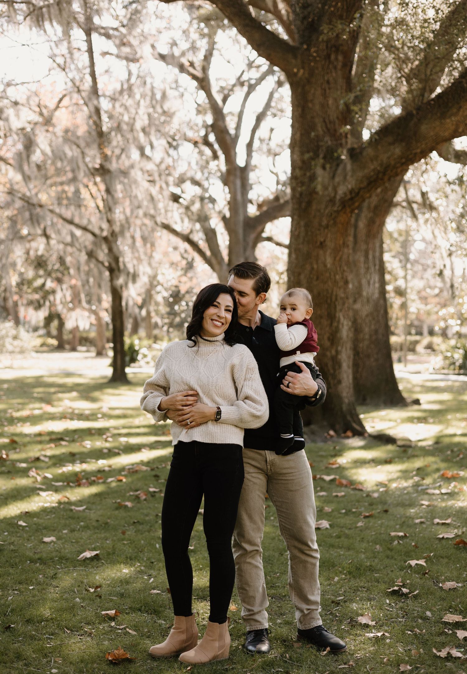 A family shares playful moments under large oak trees in a park.