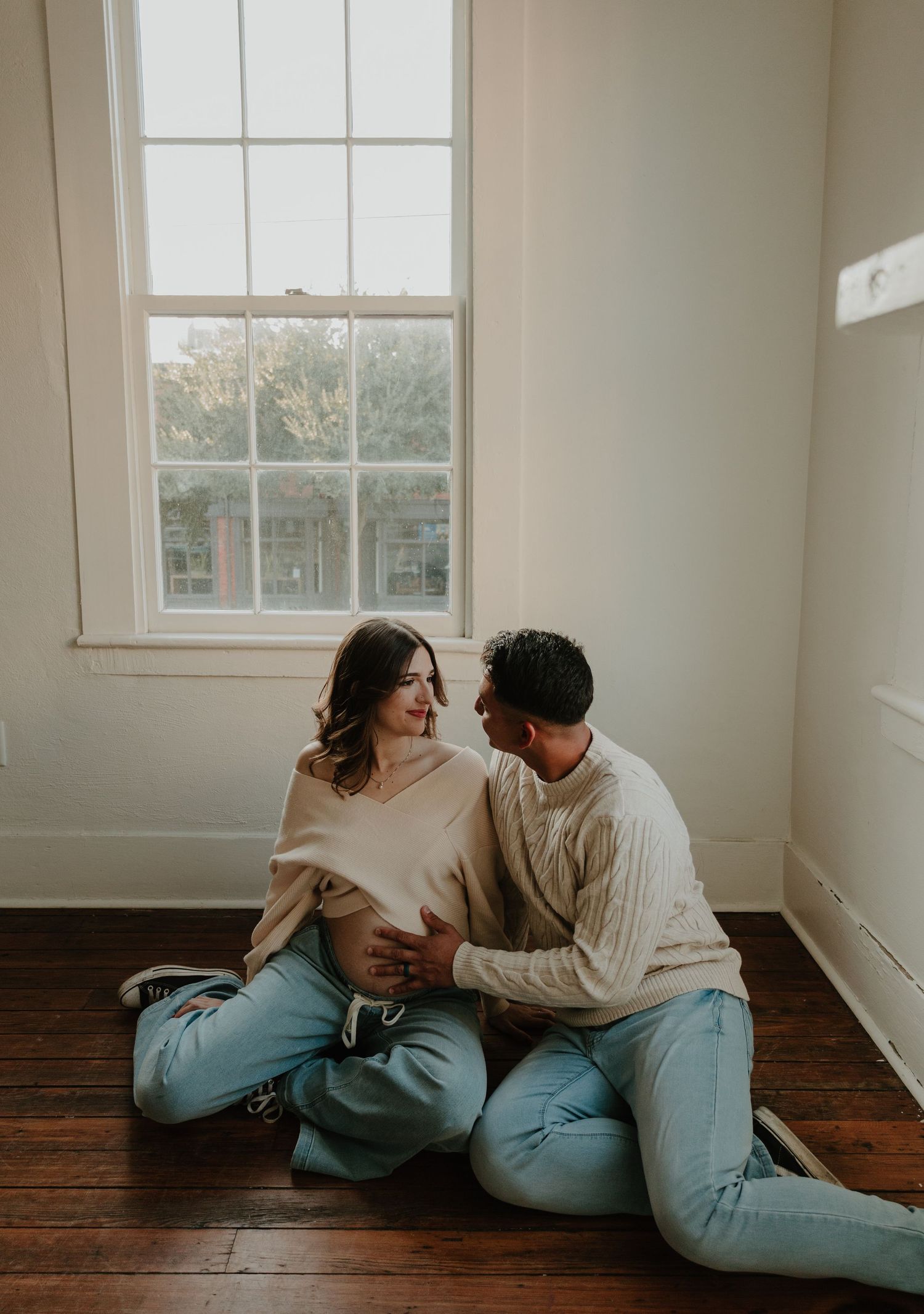 Couple in casual attire shares tender moments on hardwood floor in sunlit room.