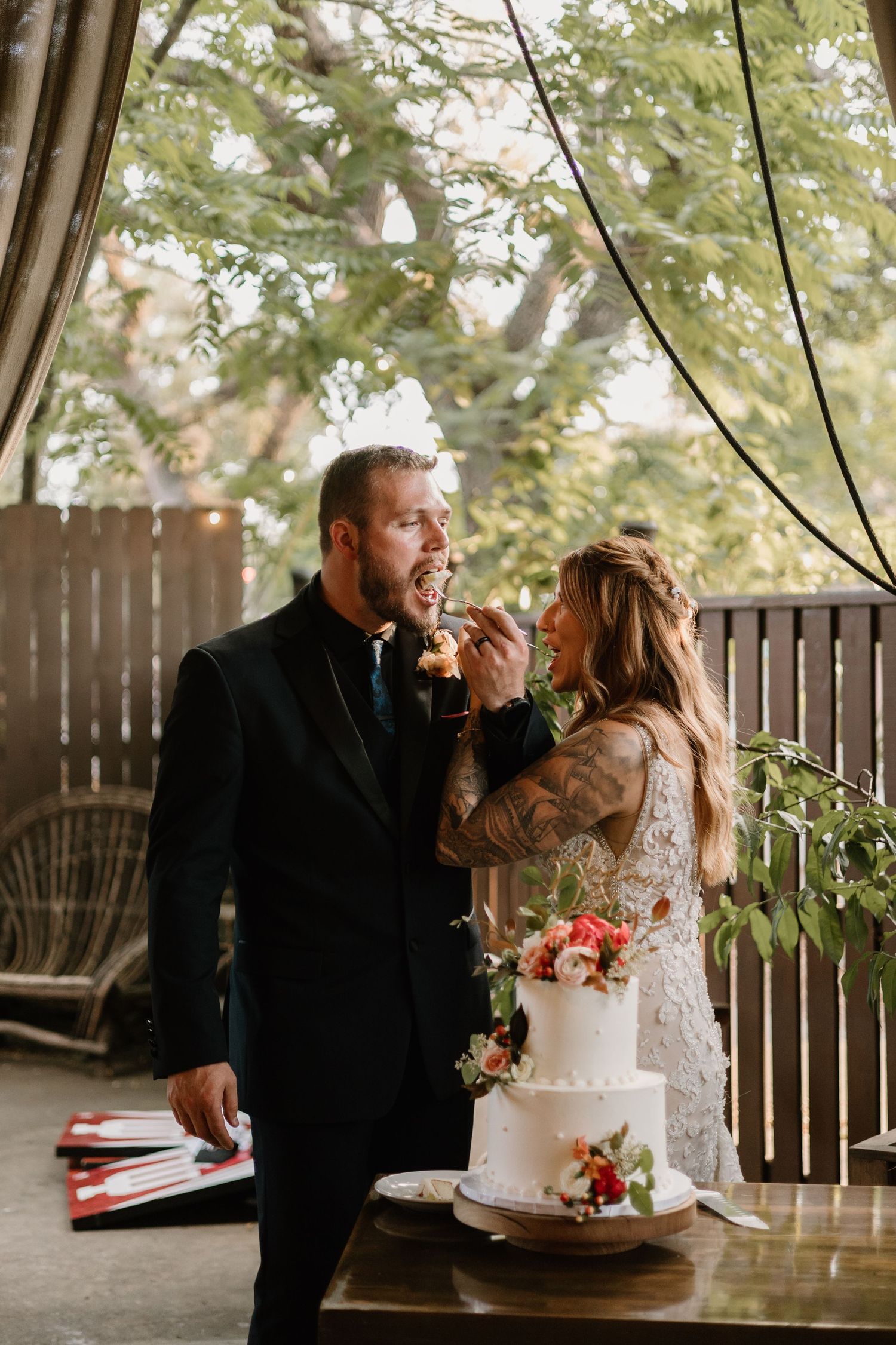A couple shares a sweet moment while cutting their white wedding cake at an outdoor reception.