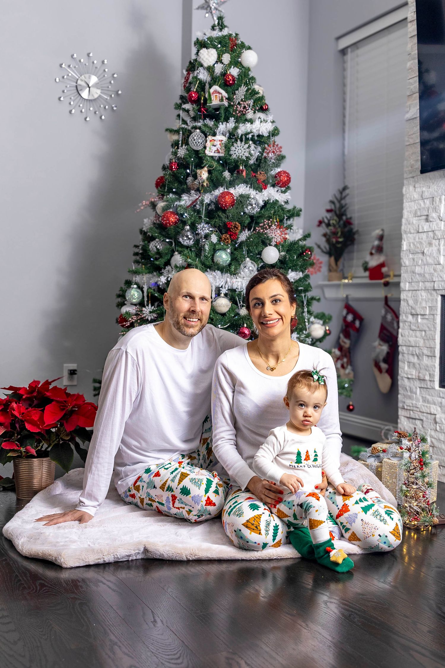 Family in matching white outfits lying on floor near Christmas tree.