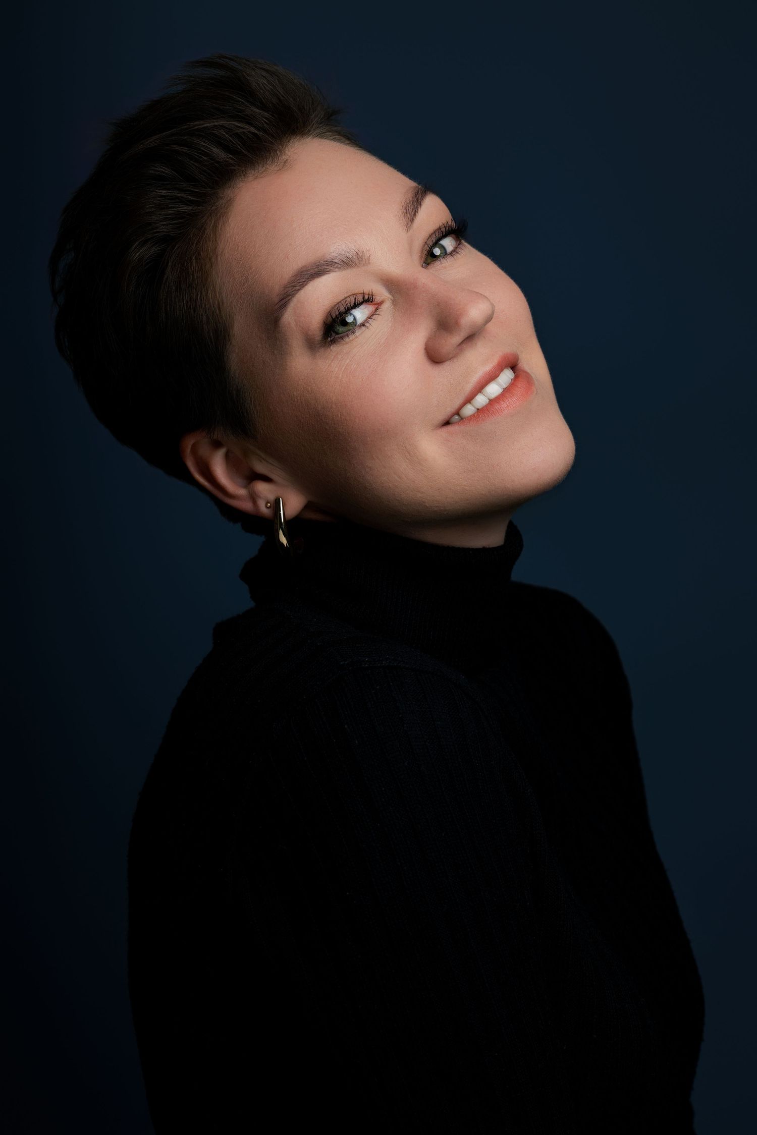 Artistic headshot with dramatic angles against deep blue background.