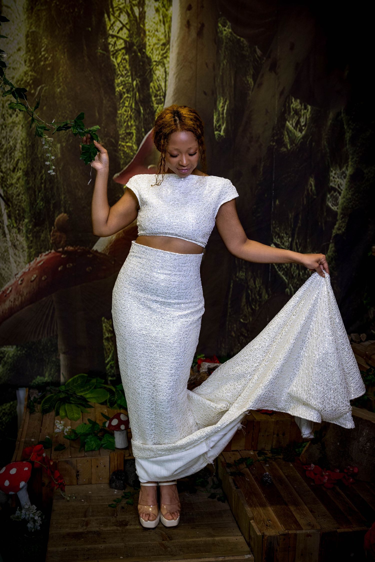 Person in sparkly white two-piece outfit dances in enchanted forest setting with dramatic lighting.