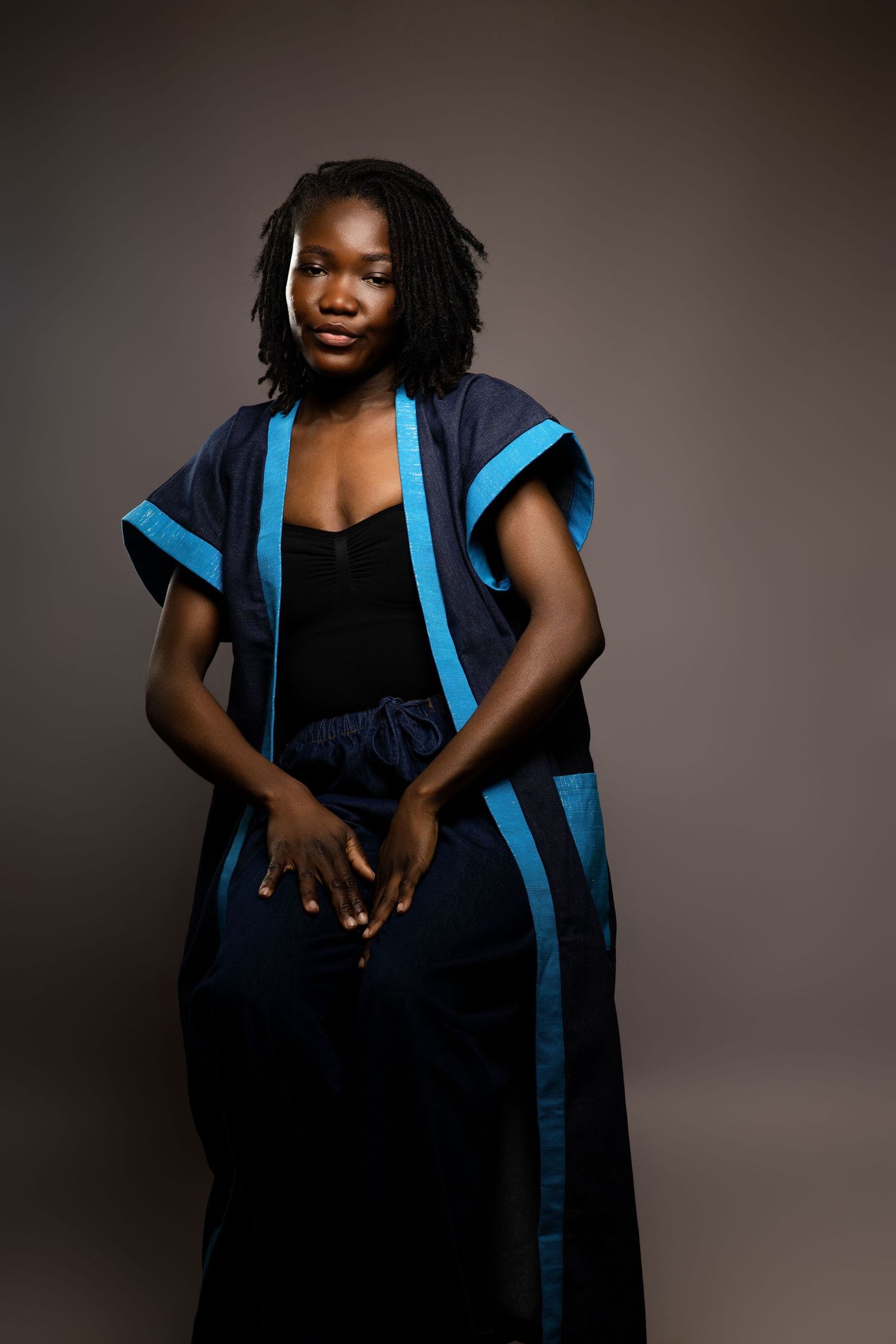 Dramatic portrait in black dress with bright blue accents against dark background.
