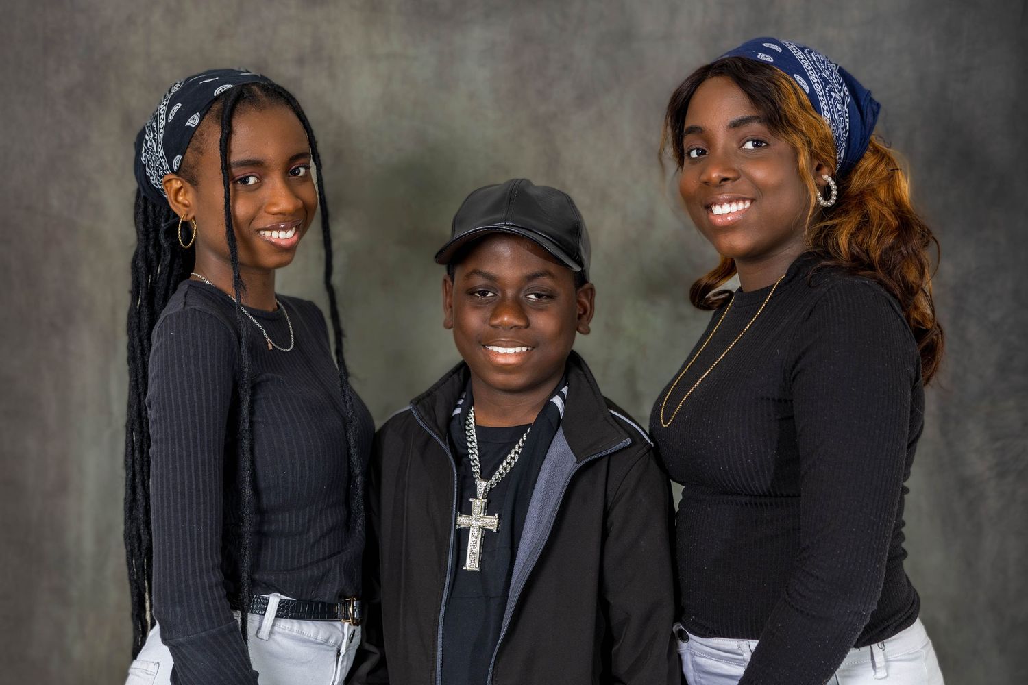 A group wearing coordinated dark outfits poses together against a textured gray background.