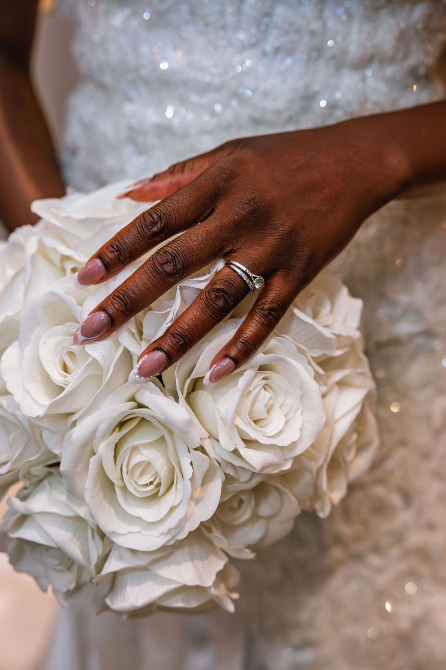 White roses and wedding rings displayed on a lace wedding dress.