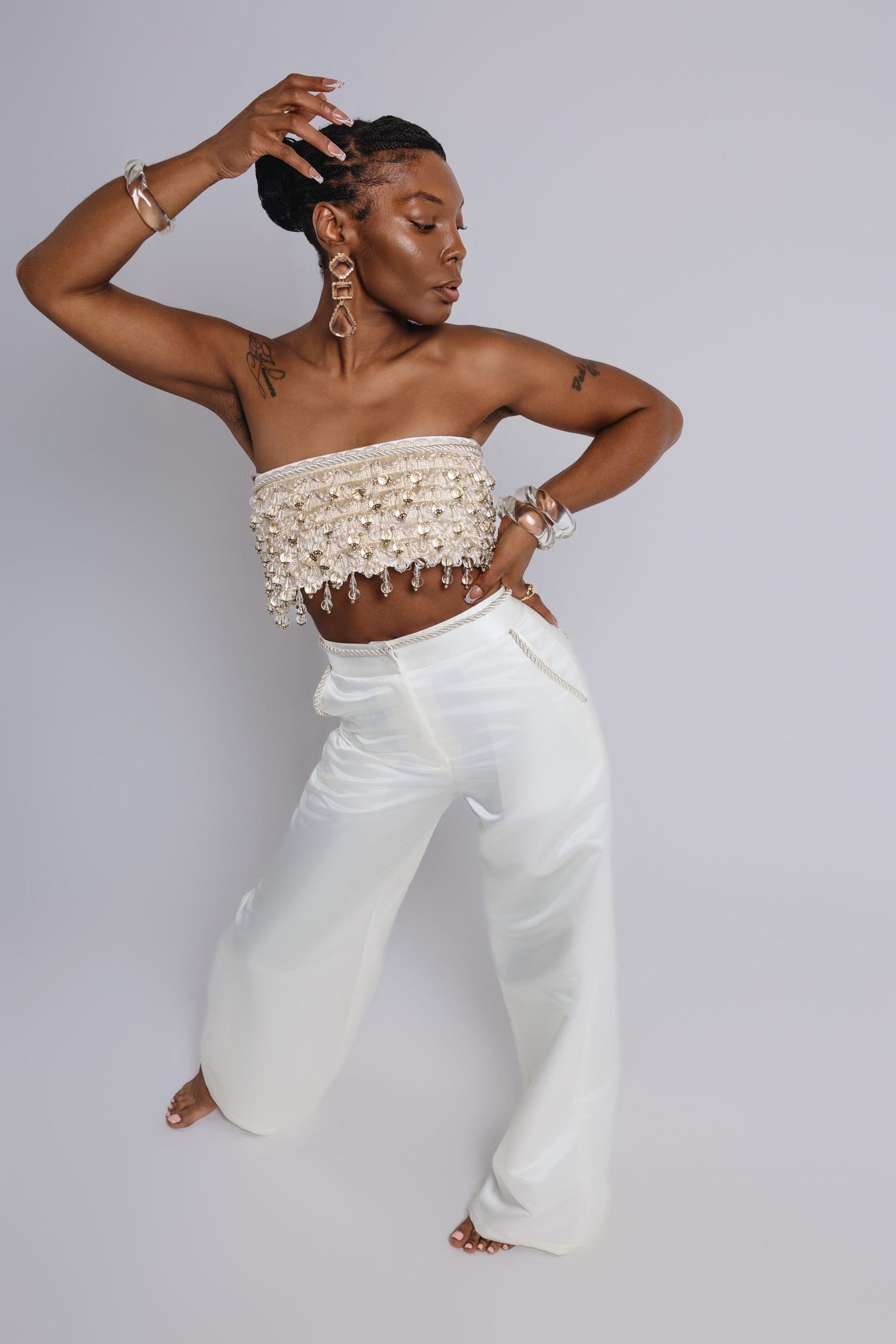 Model in white palazzo pants and crochet crop top strikes dynamic pose in studio setting.