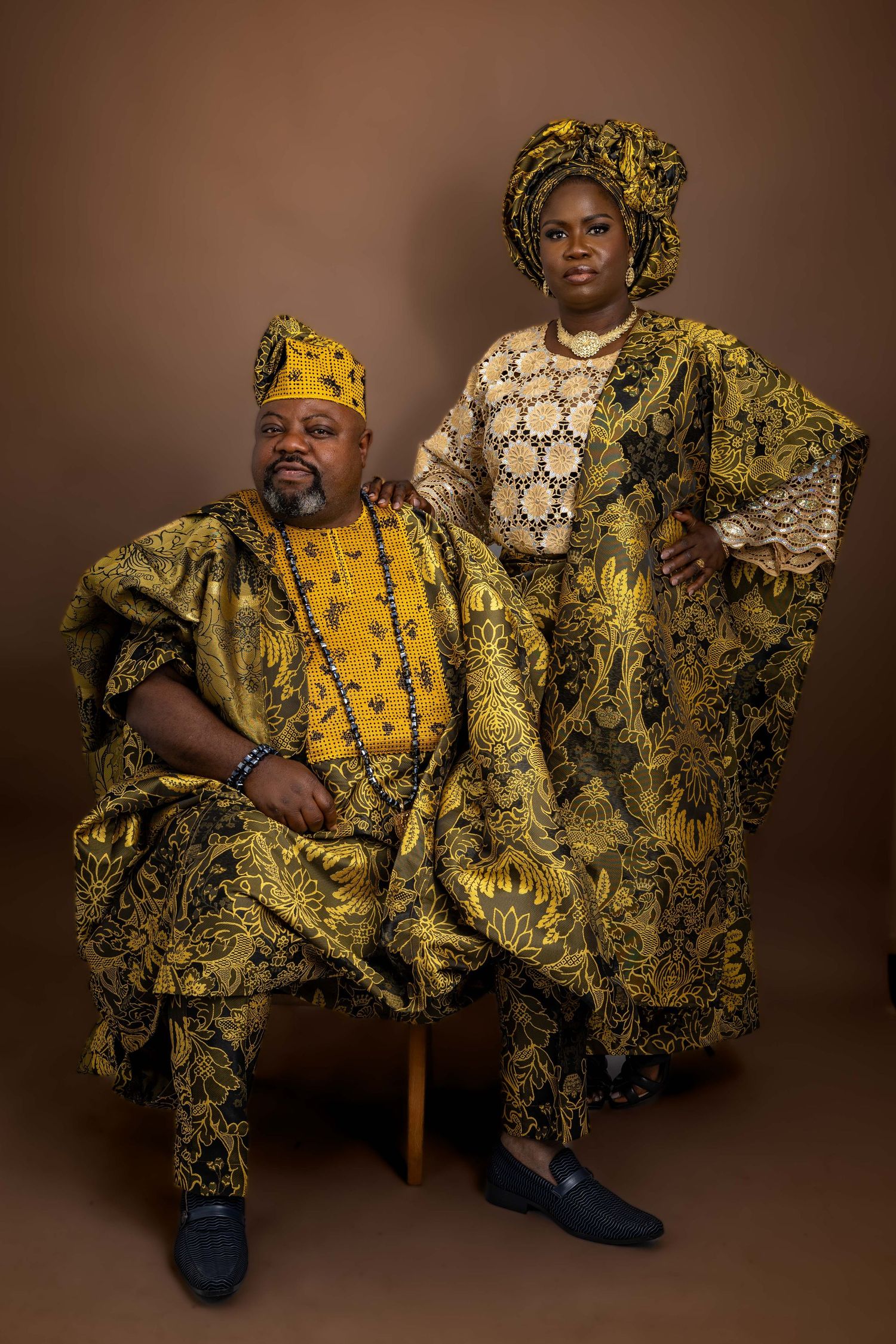 Traditional African fashion photoshoot featuring vibrant yellow and black patterned clothing against brown backdrop.