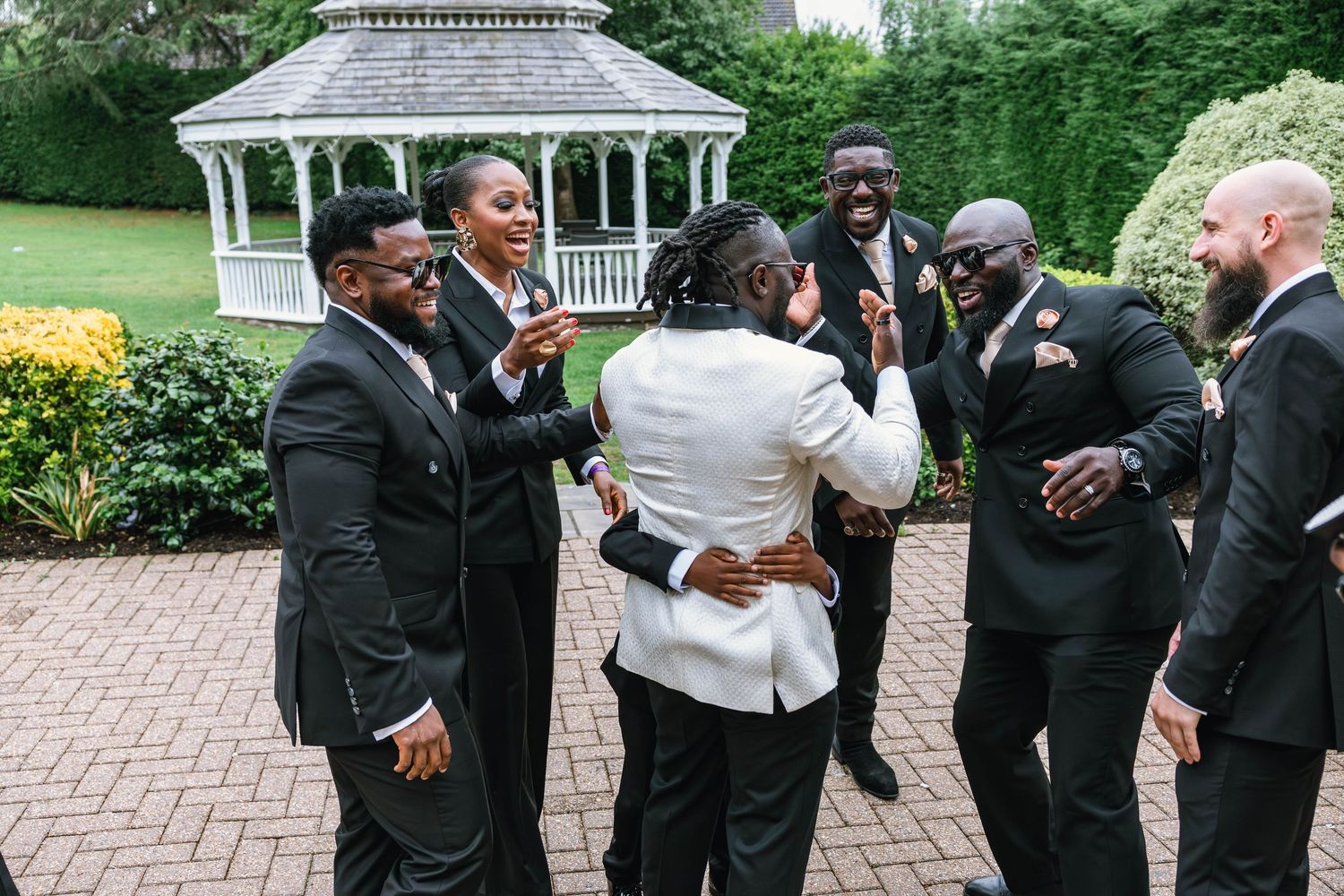 Groomsmen in black tuxedos celebrating with the wedding couple outdoors.