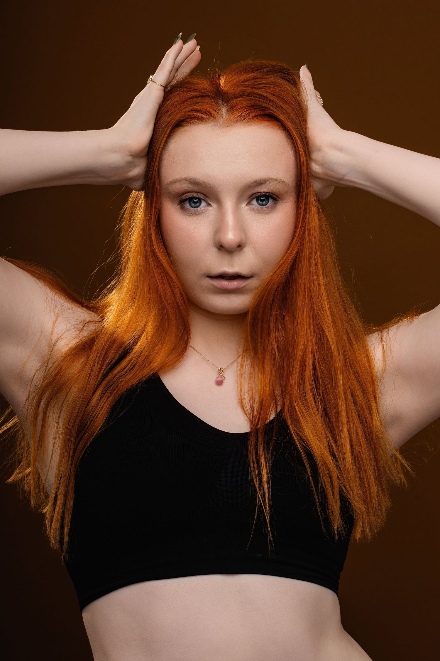 Fashion portrait with vibrant red hair against dark brown background wearing black top.