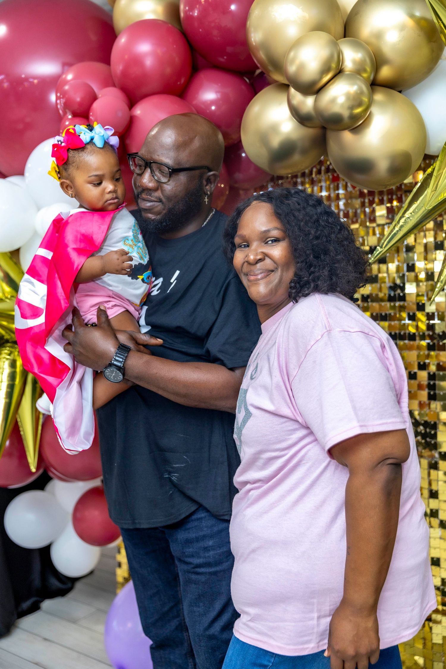A family poses together against a backdrop of red and gold balloons at a celebration.