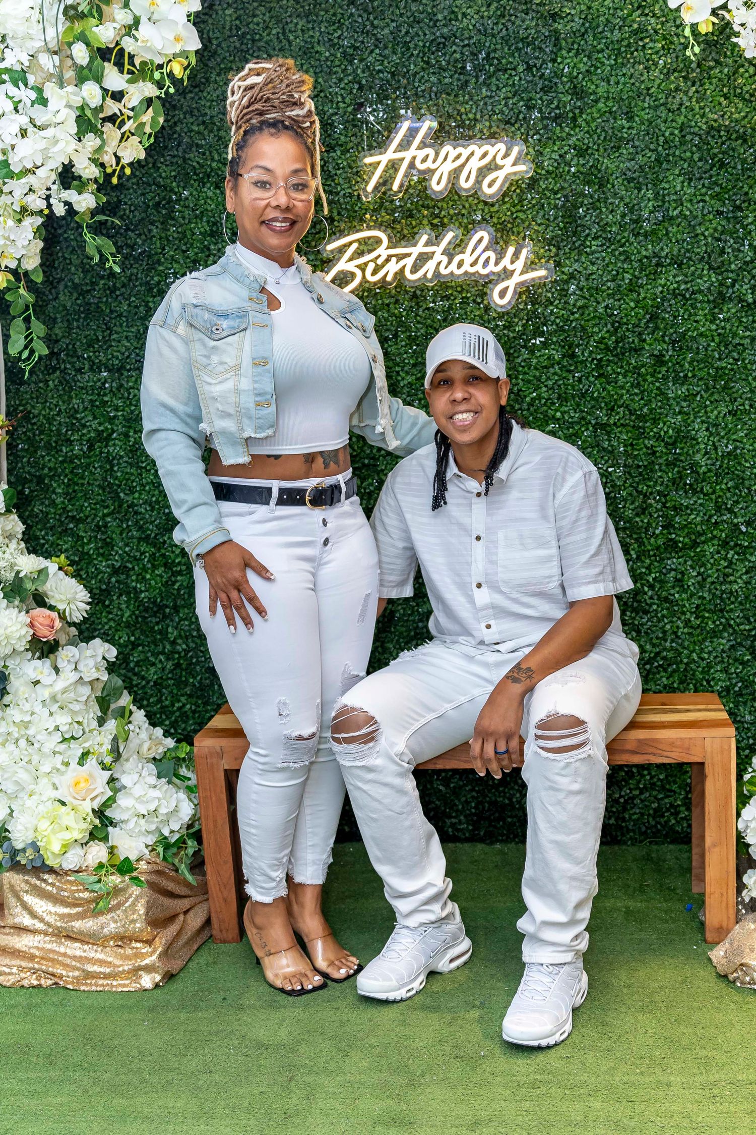 Birthday photoshoot with green hedge wall backdrop and gold 'Happy Birthday' sign.