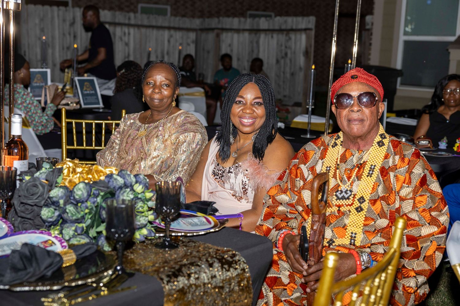 Three guests enjoying a formal dinner event at a decorated table with floral centerpieces.