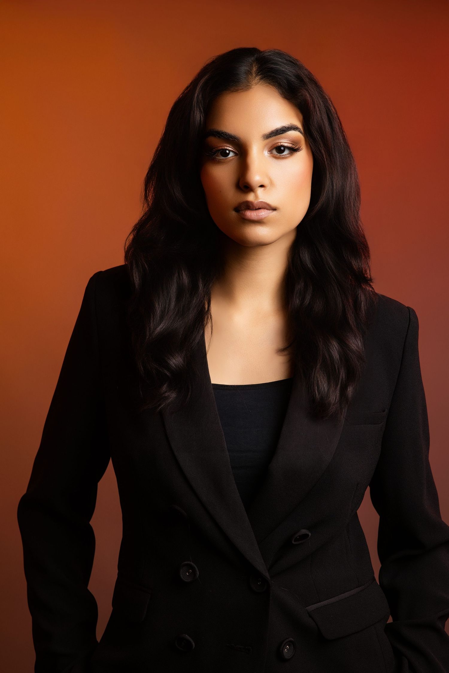 Professional studio portrait series showing dramatic lighting and a black blazer against a dark red background.