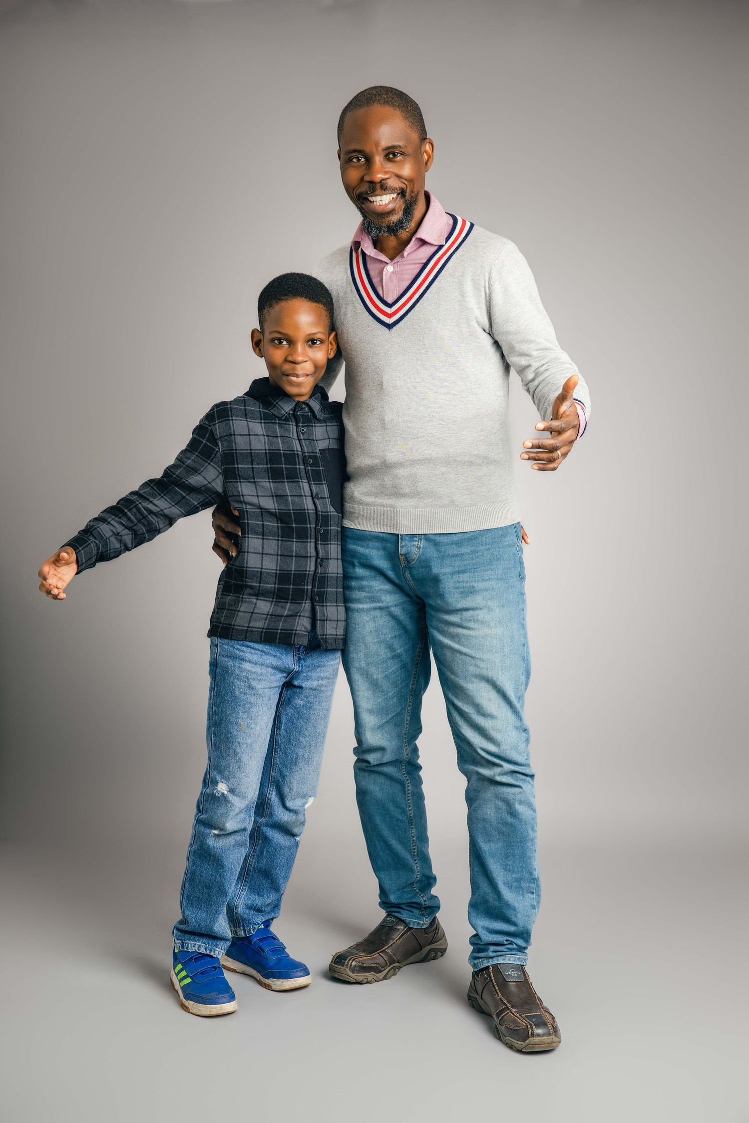 Parent and child posing together in casual denim outfits against grey background.