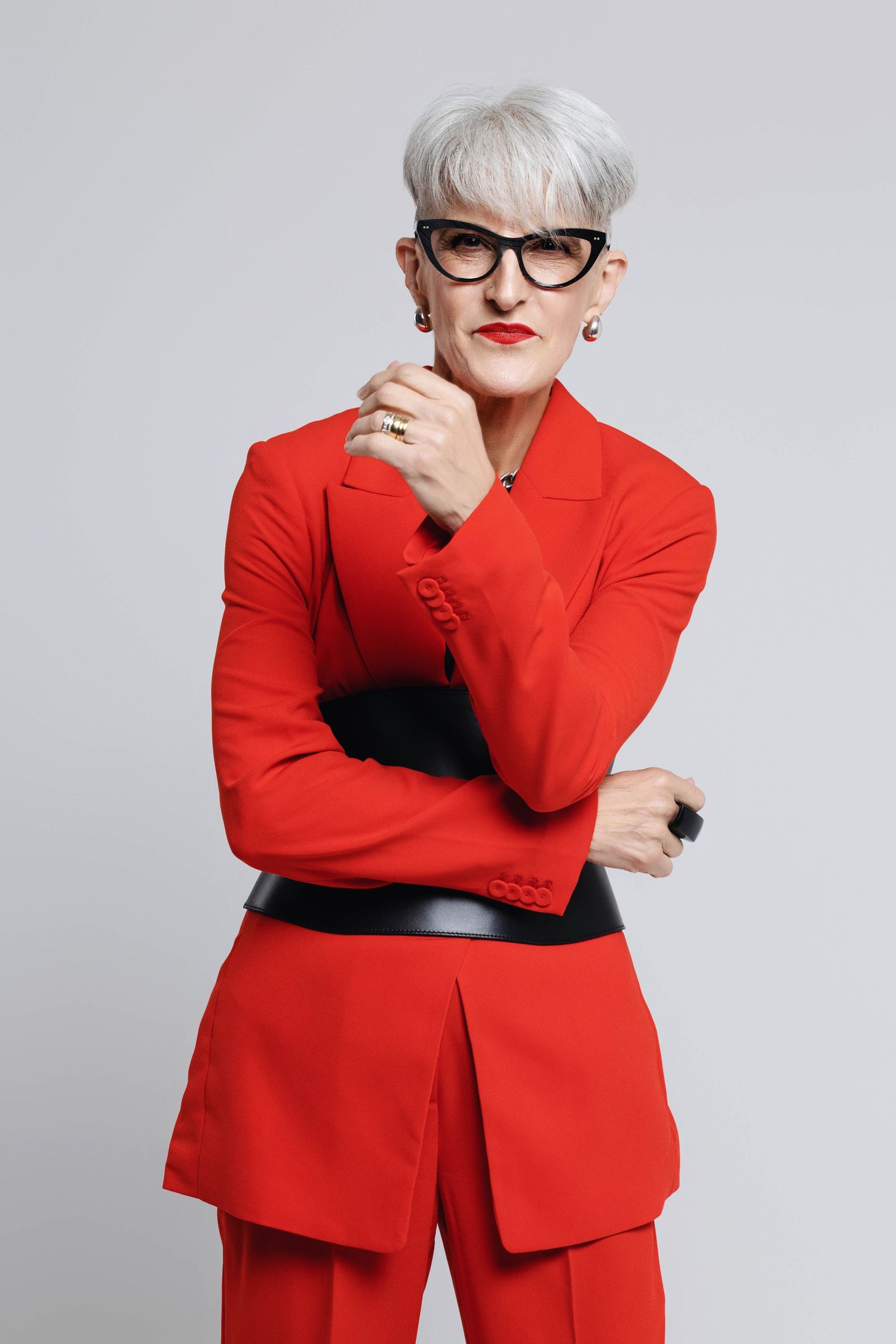 A figure in a vibrant red blazer and black belt poses confidently against a light gray background.