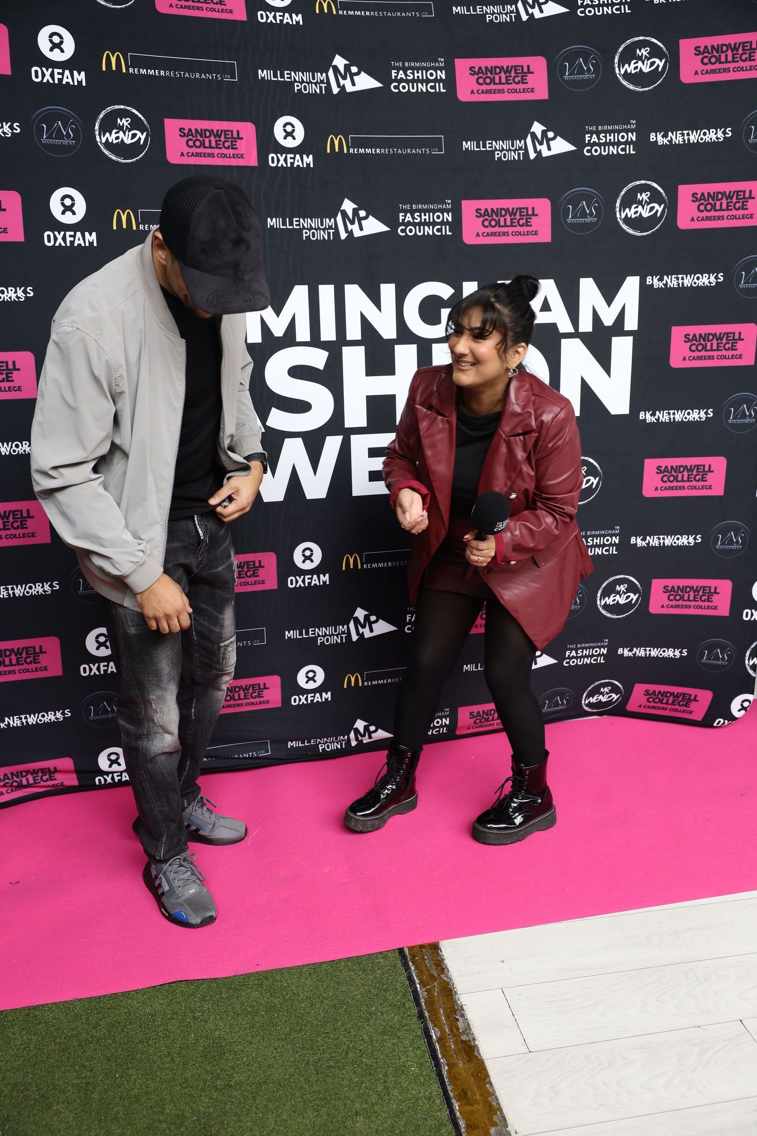 People posing on a pink carpet with event sponsor backdrop at a fashion show.