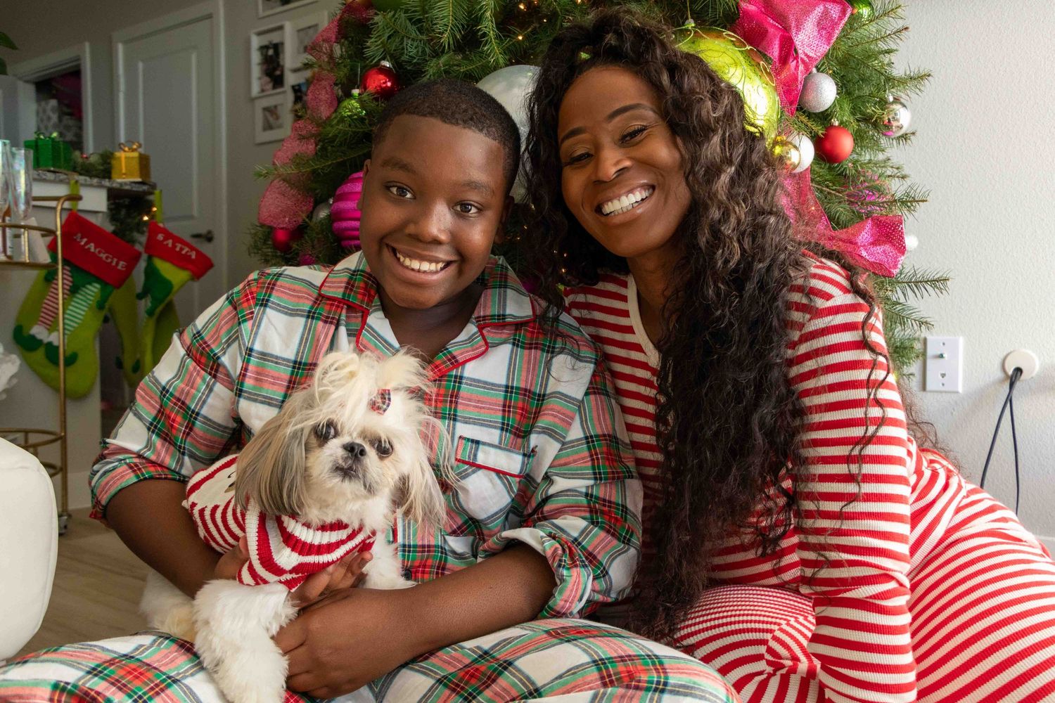 Holiday family photo with dog featuring people in red striped shirts and plaid by Christmas tree.