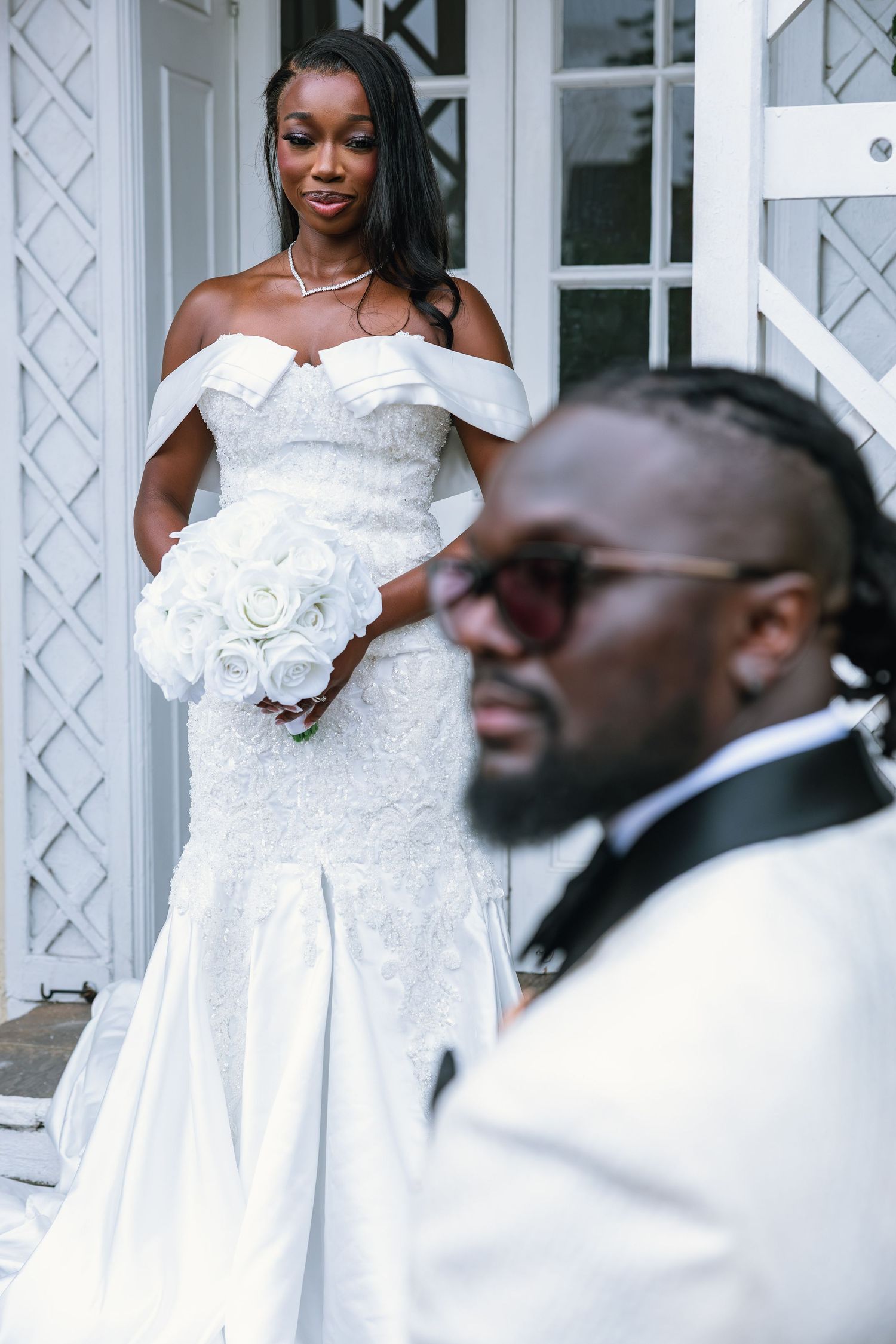 Wedding couple posing in elegant white attire against white lattice backdrop.