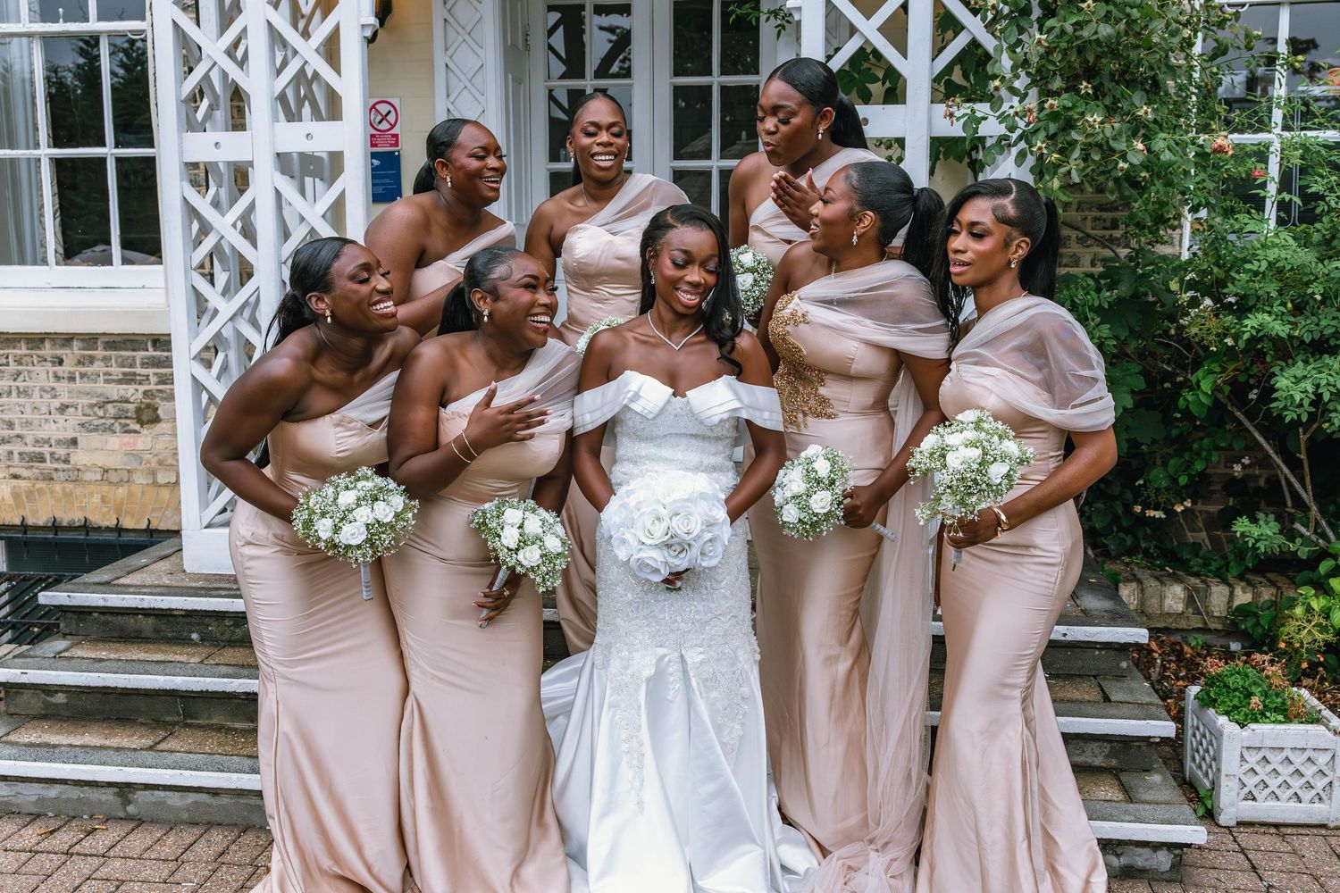 Wedding party in pink and white attire posing together outside a venue.