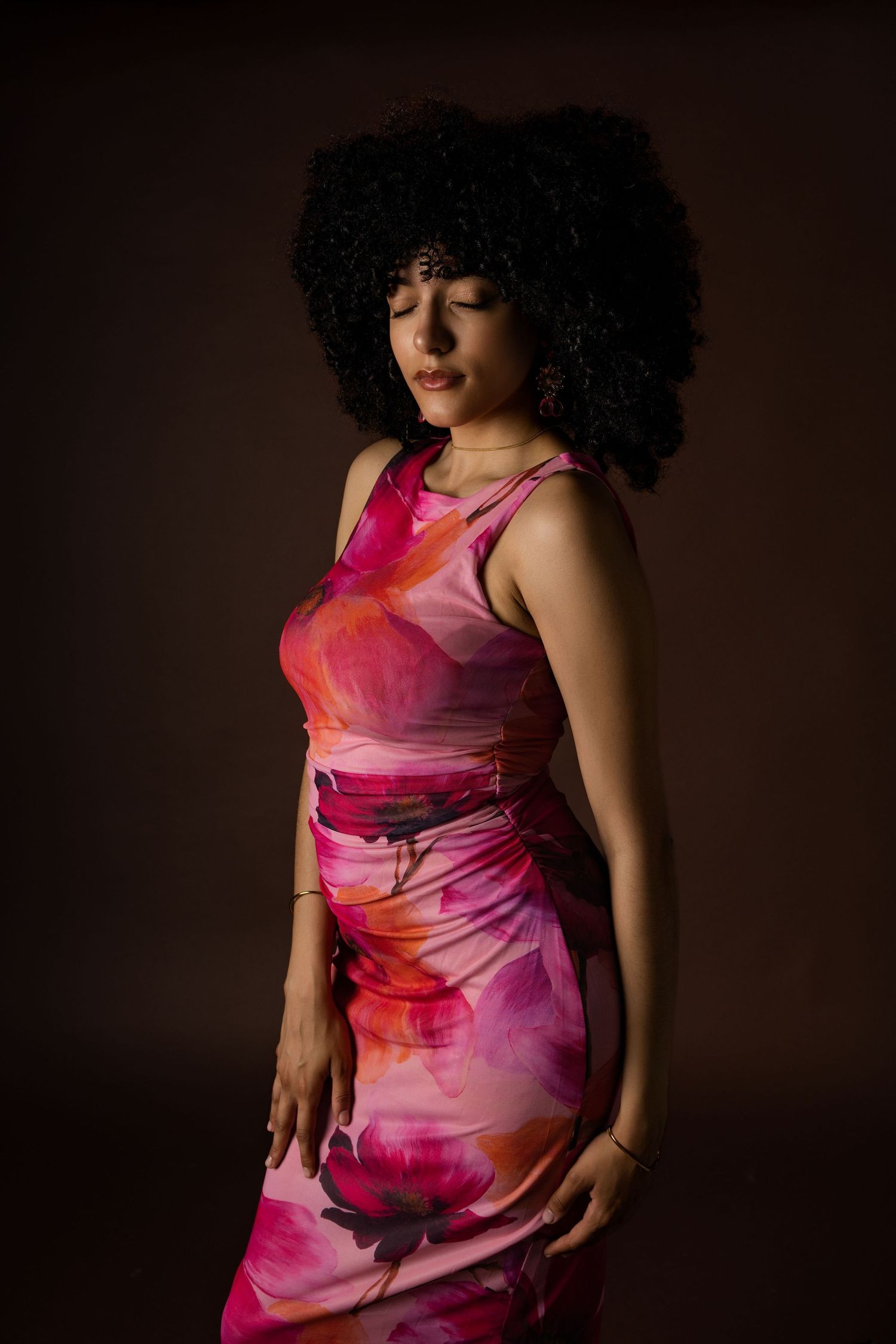Fashion portrait of a woman in pink floral dress with natural curly hair against dark background.