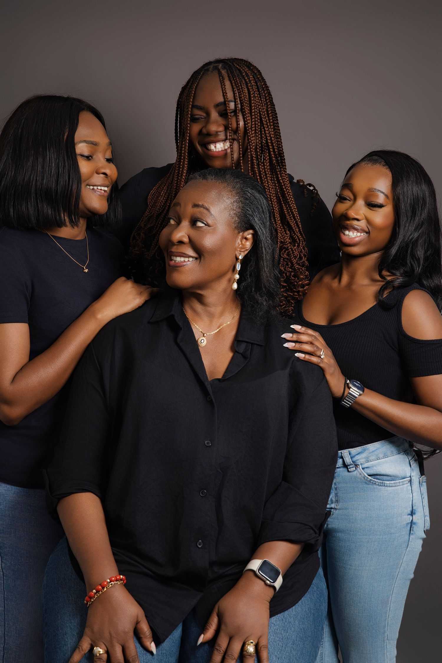 Three friends in black tops and jeans share joyful candid moments against a dark background in a photo series.