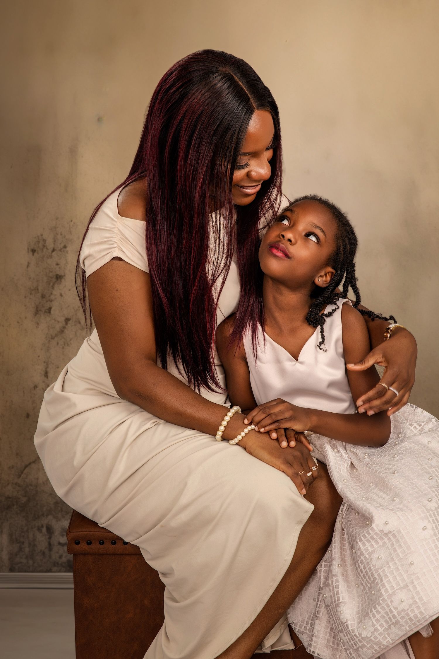 A heartwarming series of candid moments between a parent and child wearing white dresses against a textured backdrop.