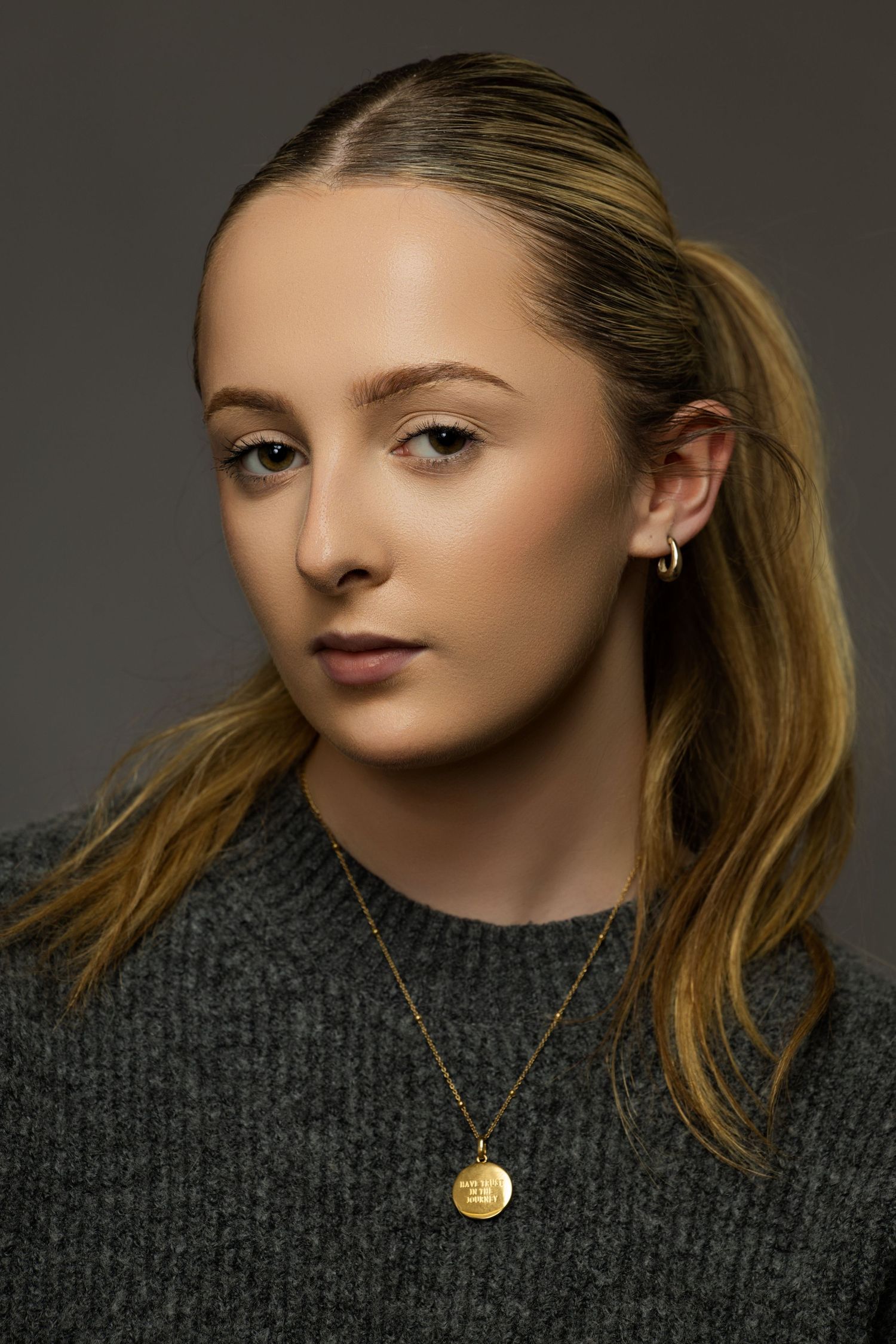 Fashion portrait of model in gray sweater wearing delicate gold pendant necklace.