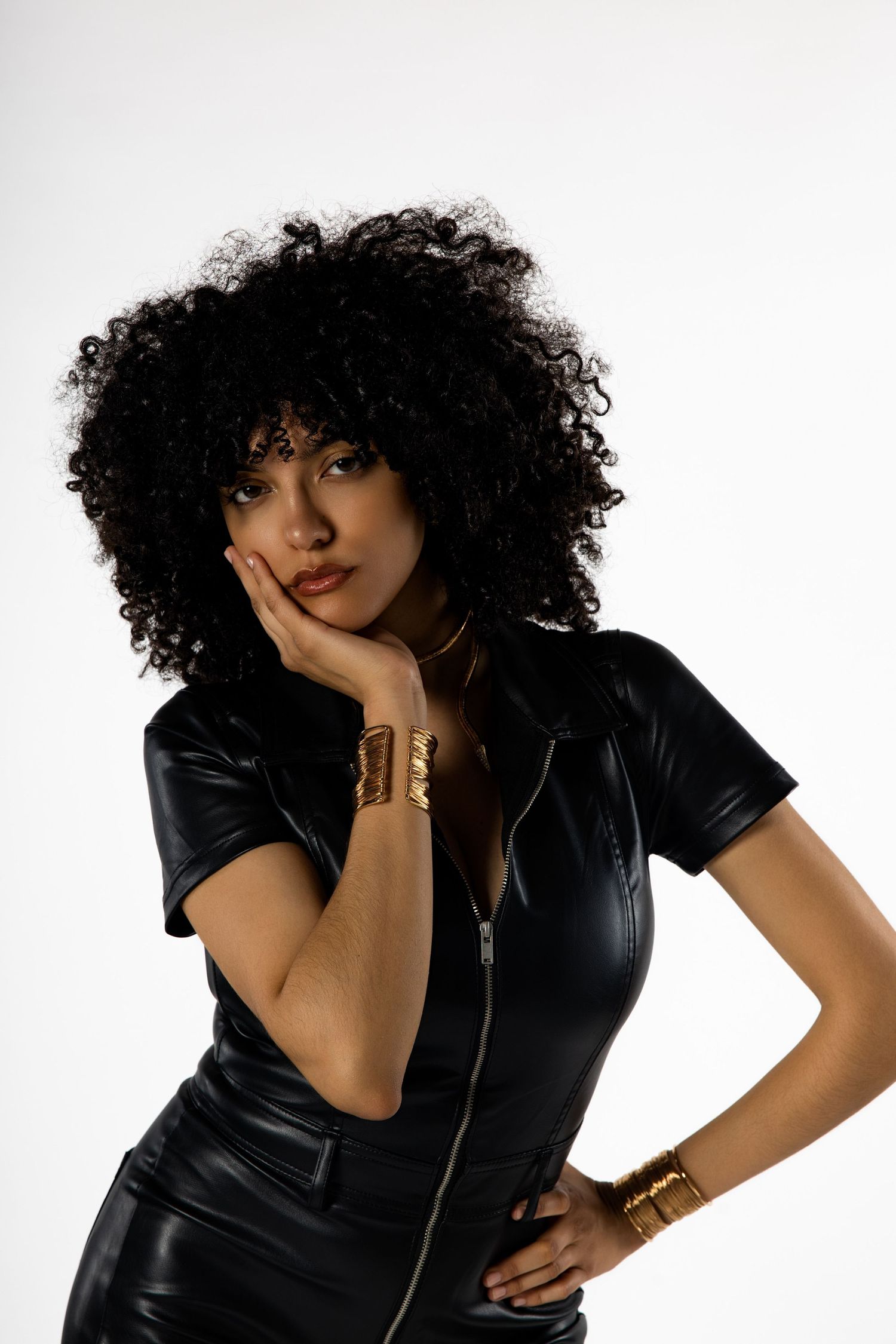 Fashion series in black leather outfit with voluminous curly hair against white background.