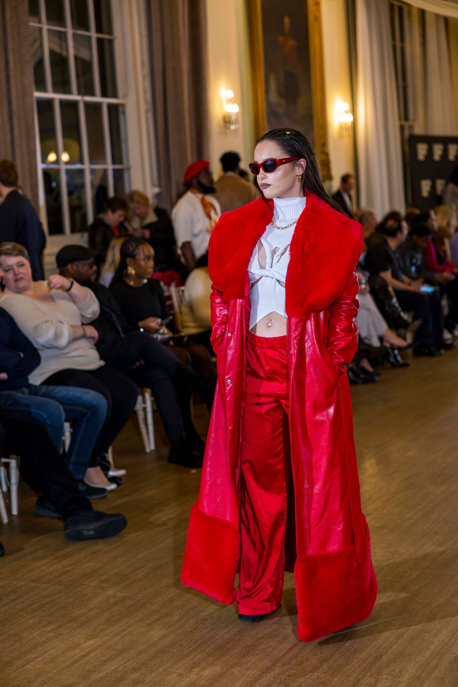 Model walking runway in dramatic red ensemble with white ruffled details at fashion show.