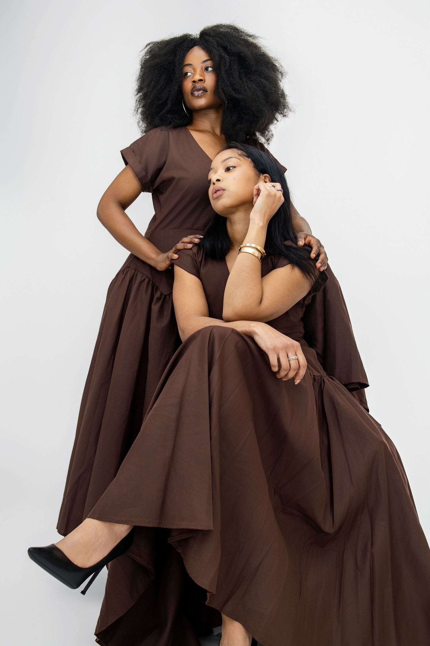 Fashion model in flowing brown dress poses gracefully against white background in artistic photoshoot series.