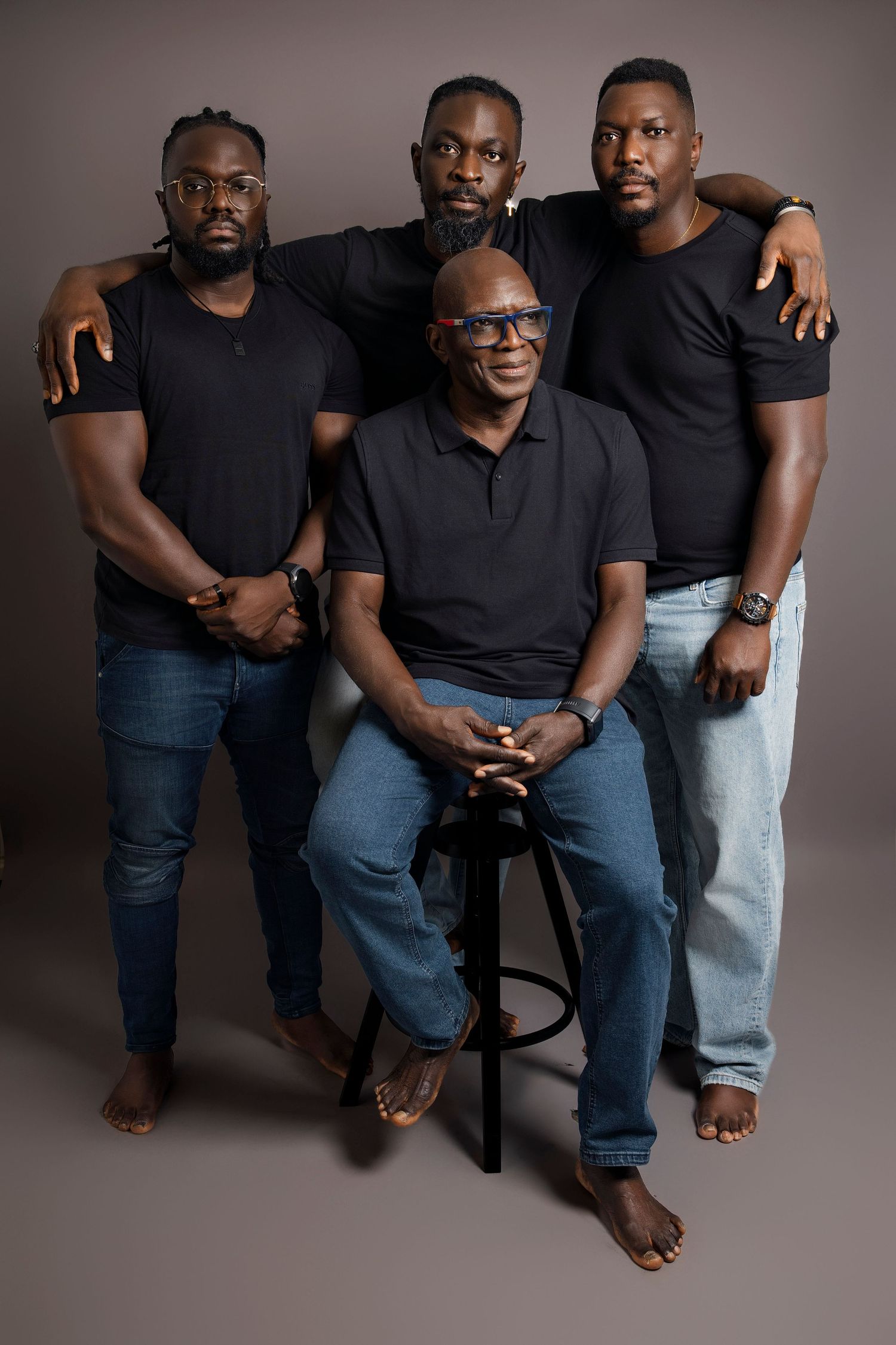 Studio portrait of four men in casual black tops and jeans against neutral background.
