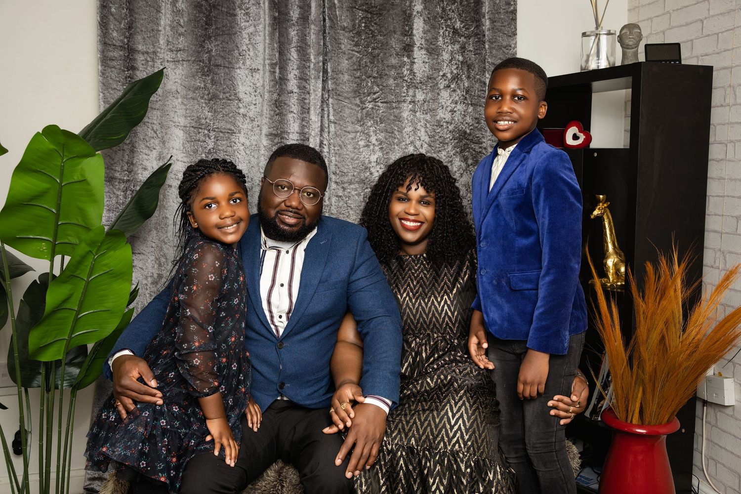A family group in coordinated formal attire poses together against a sparkly backdrop with plants.