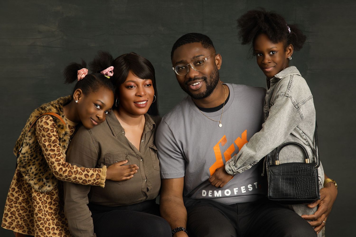 A family group poses together in casual attire against a dark studio backdrop.