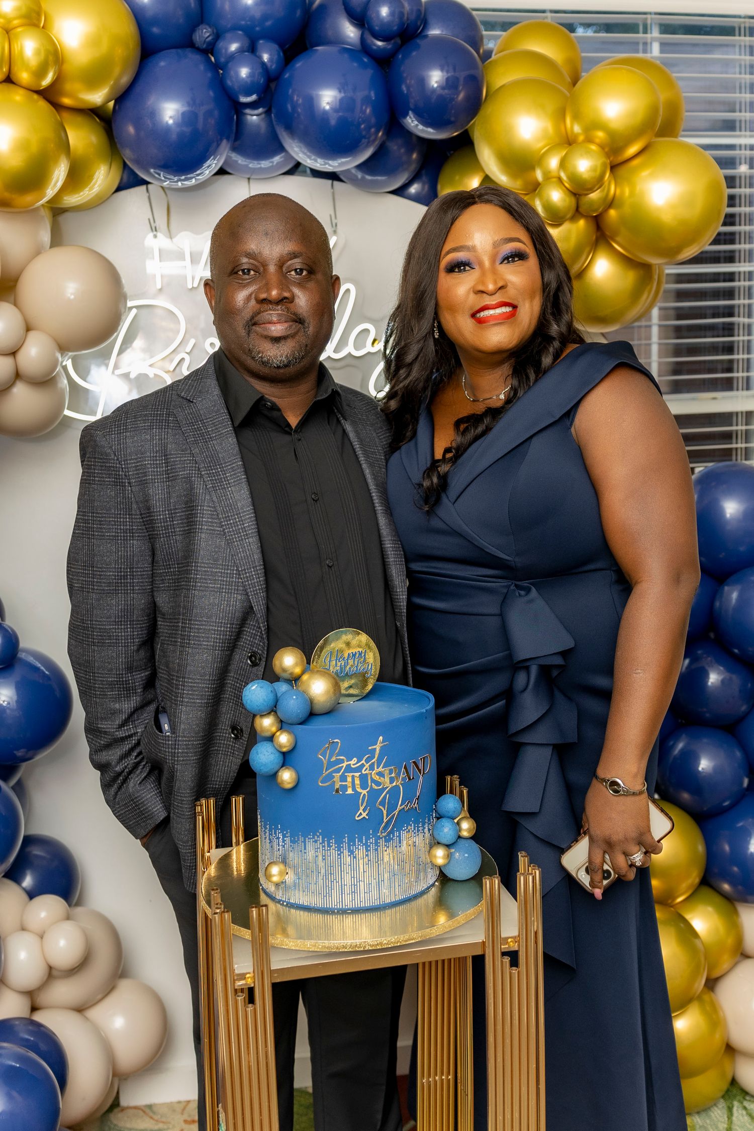 Celebration setup with blue and gold balloon arch decorations against a white backdrop.