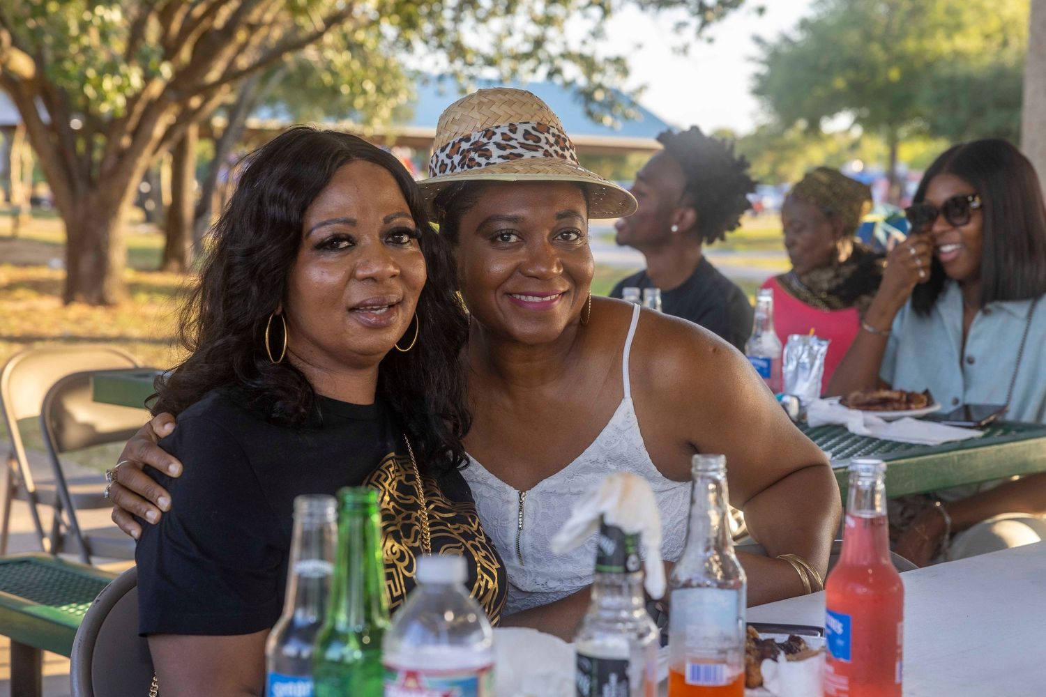 Two friends wearing a tiara and casual attire smile at an outdoor table.