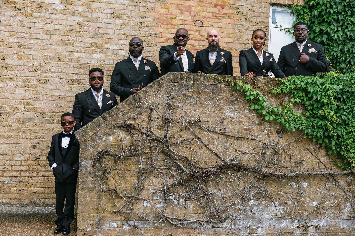 Wedding party posed against historic brick wall with ivy.