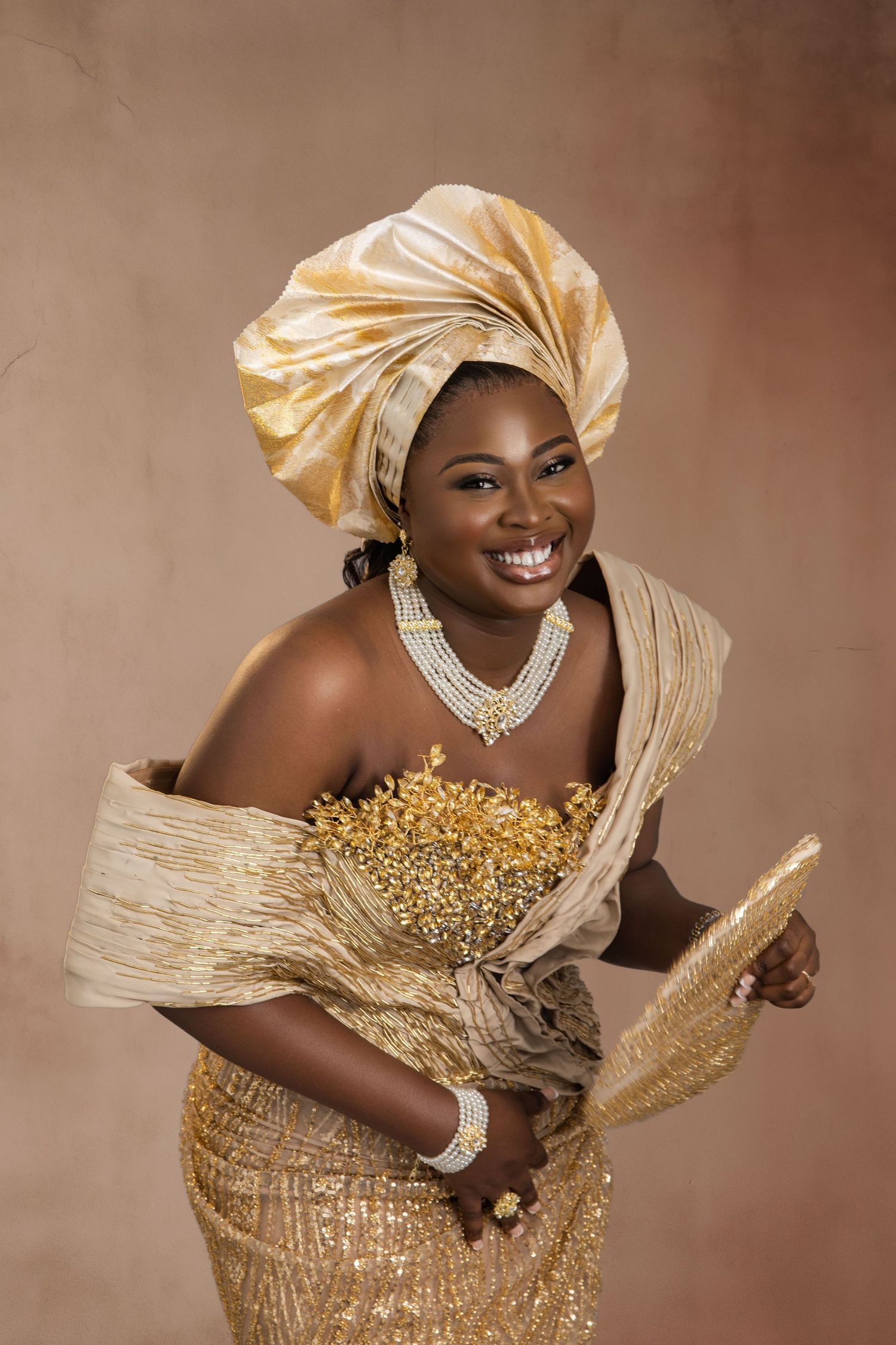 Portrait of a joyful woman in traditional gold African attire with gele headwrap and beaded necklace.