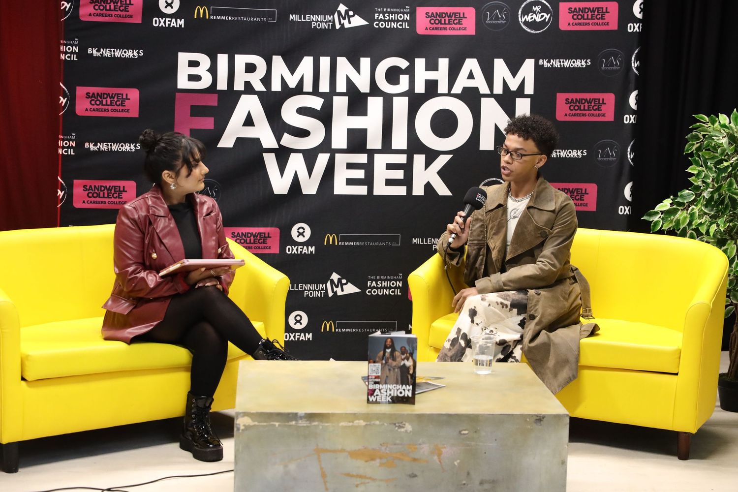 Birmingham Fashion Week event space with black backdrop and yellow seating arrangements.