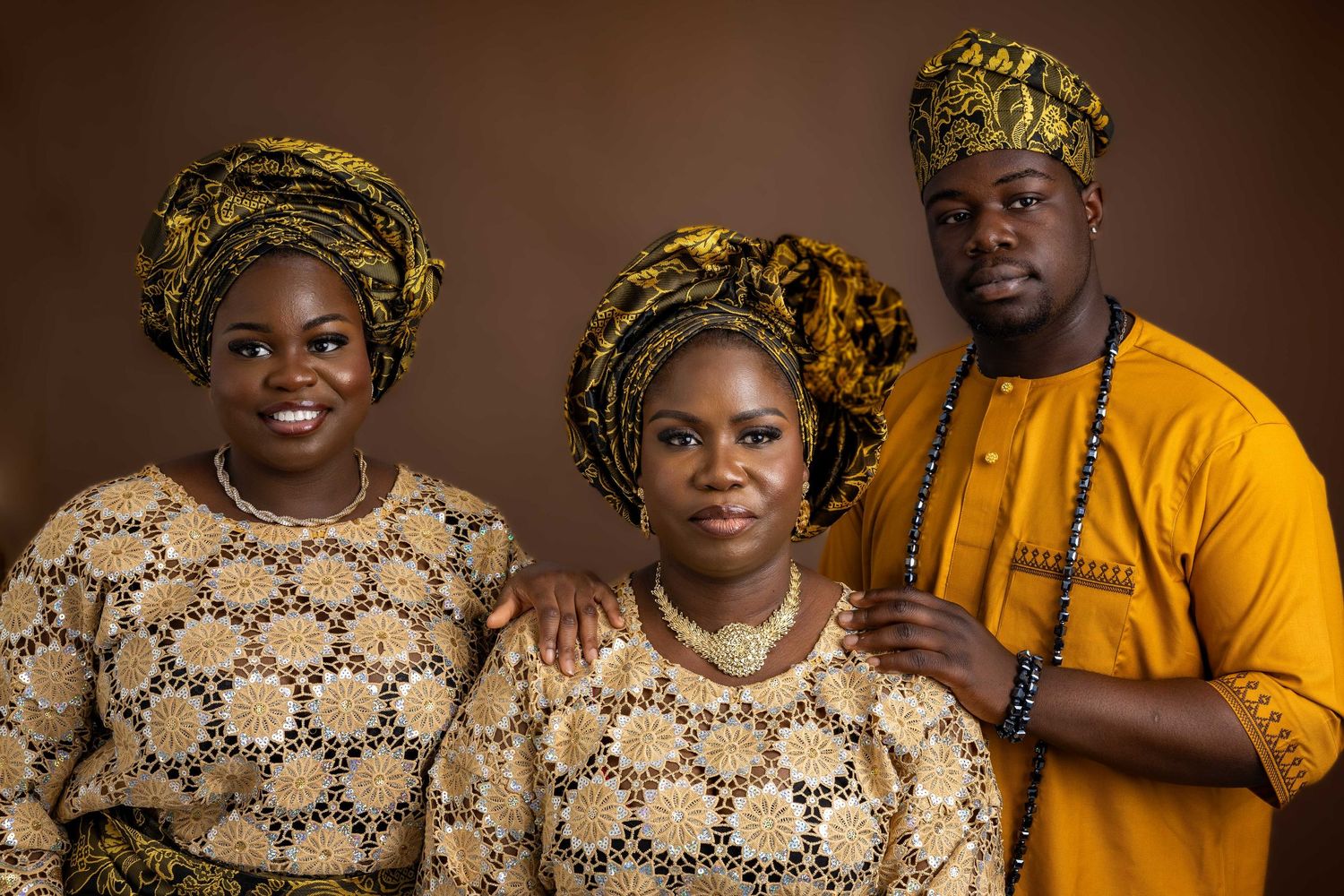 Three people in matching yellow and brown traditional African formal wear pose for portrait.