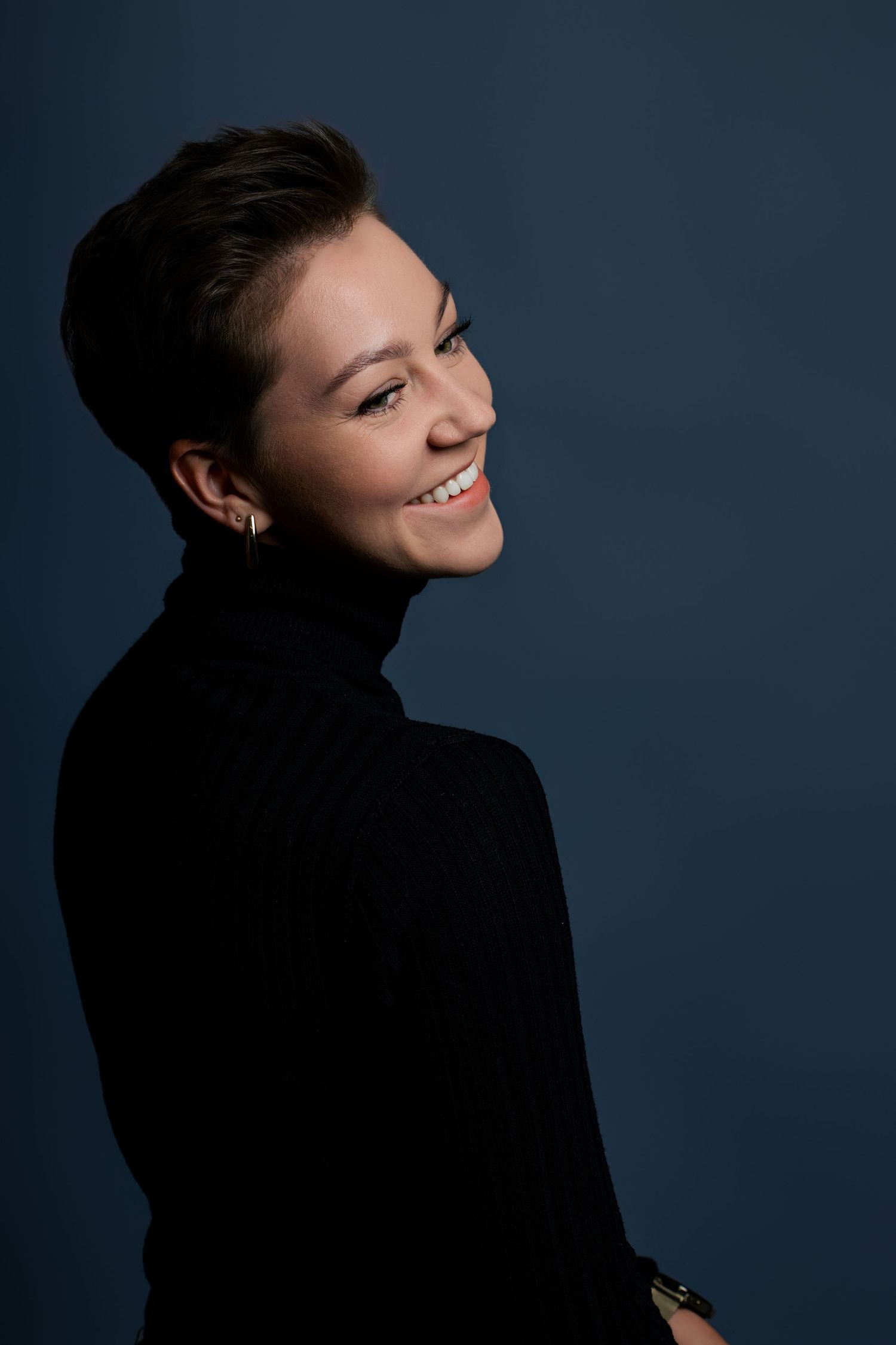 Side profile portrait of a person in black turtleneck smiling against dark background.